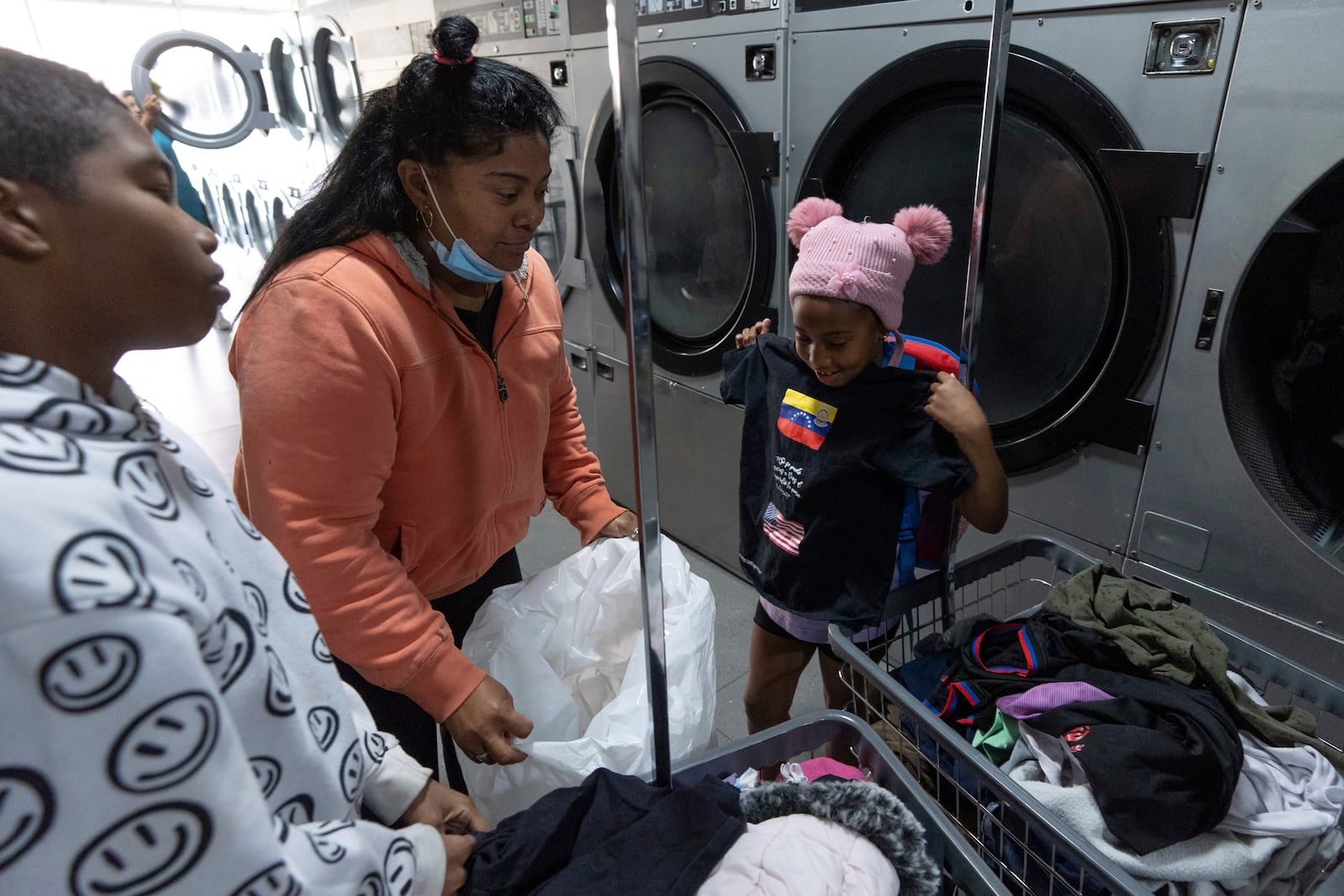 Margelis Rodriguez, of Venezuela, center, looks at her 6-year-old daughter Maickeliys holding a shirt with the flags of Venezuela and the United States, and the Spanish message: "Yes it was possible, thank God. The wait was worth it. I made it!" at the laundromat near the migrant shelter where they are staying in Tijuana, Mexico, Friday, Jan. 31, 2025. (AP Photo/Gregory Bull)