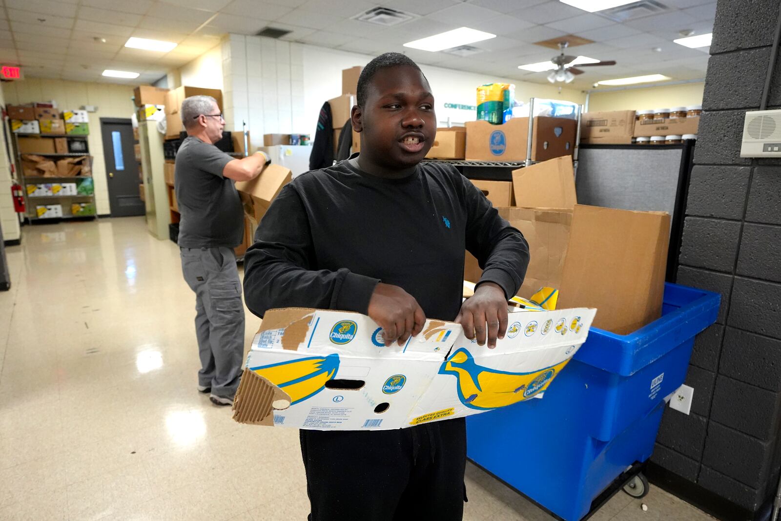 Volunteer Chris Hawn, of Providence, R.I., front, tears cardboard boxes in a food pantry at Federal Hill House, Tuesday, Nov. 12, 2024, in Providence, R.I. (AP Photo/Steven Senne)