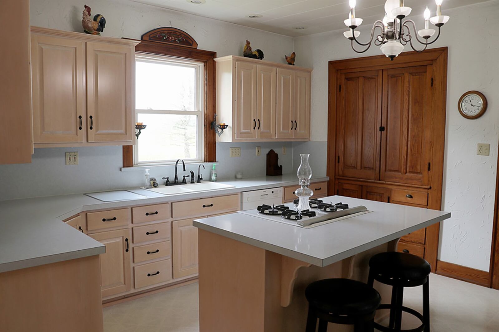 The spacious kitchen has light cabinetry and white countertops. A window is above the sink, and an island has a gas range with retractable vent and breakfast bar seating for two. A wall has the original built-in storage cabinets and drawers. CONTRIBUTED PHOTO BY KATHY TYLER