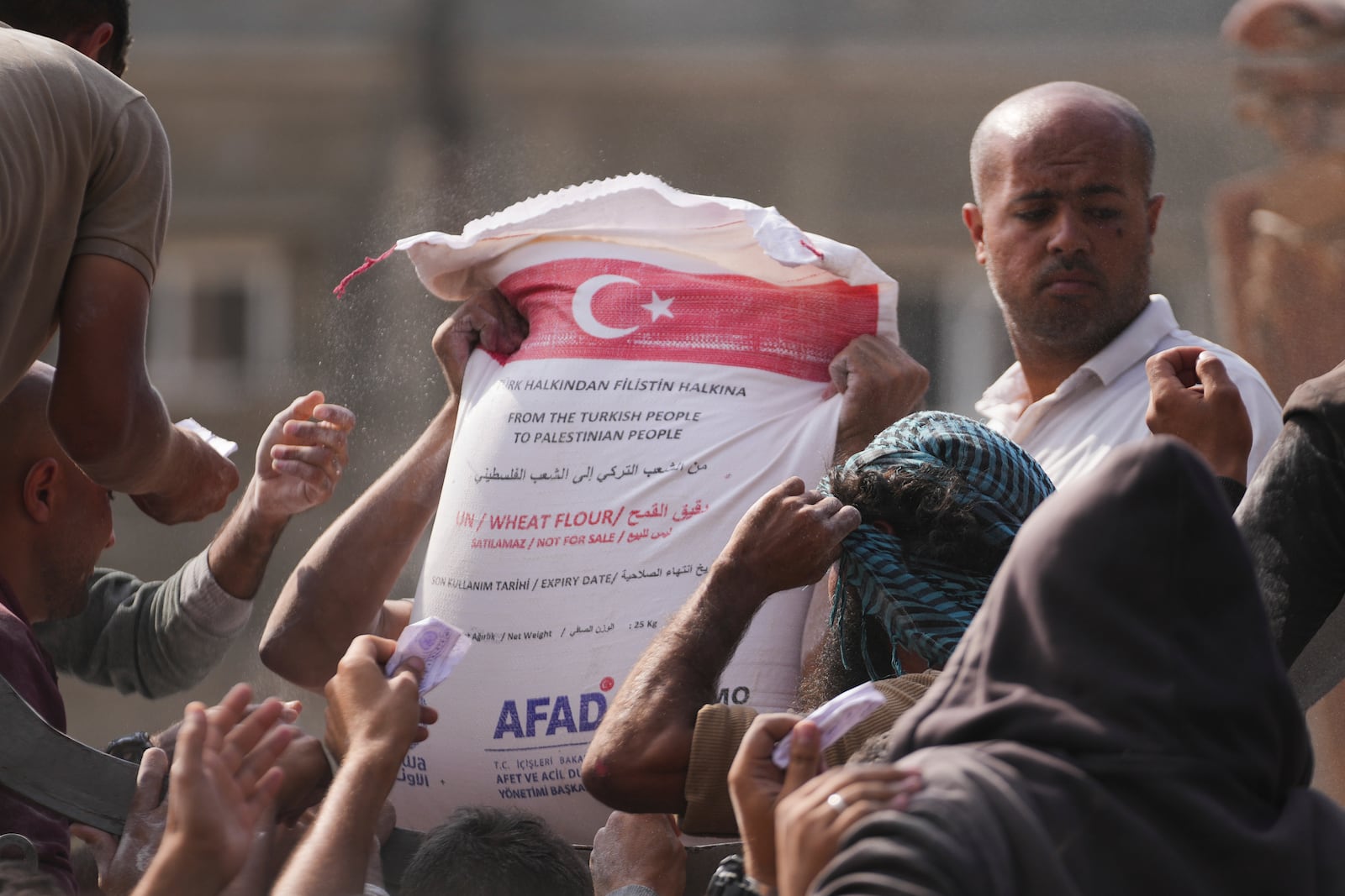 Palestinians gather to receive bags of flour distributed by UNRWA, the U.N. agency helping Palestinian refugees, in Deir al Balah, central Gaza Strip, Saturday, Nov. 2, 2024. (AP Photo/Abdel Kareem Hana)