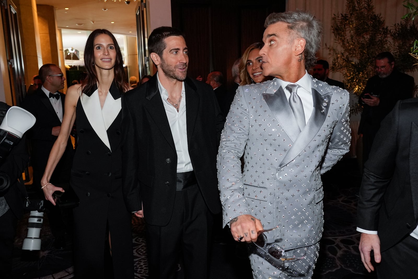 Jeanne Cadieu, from left, Jake Gyllenhaal, and Robbie Williams arrive at the 82nd Golden Globes on Sunday, Jan. 5, 2025, at the Beverly Hilton in Beverly Hills, Calif. (AP Photo/Chris Pizzello)