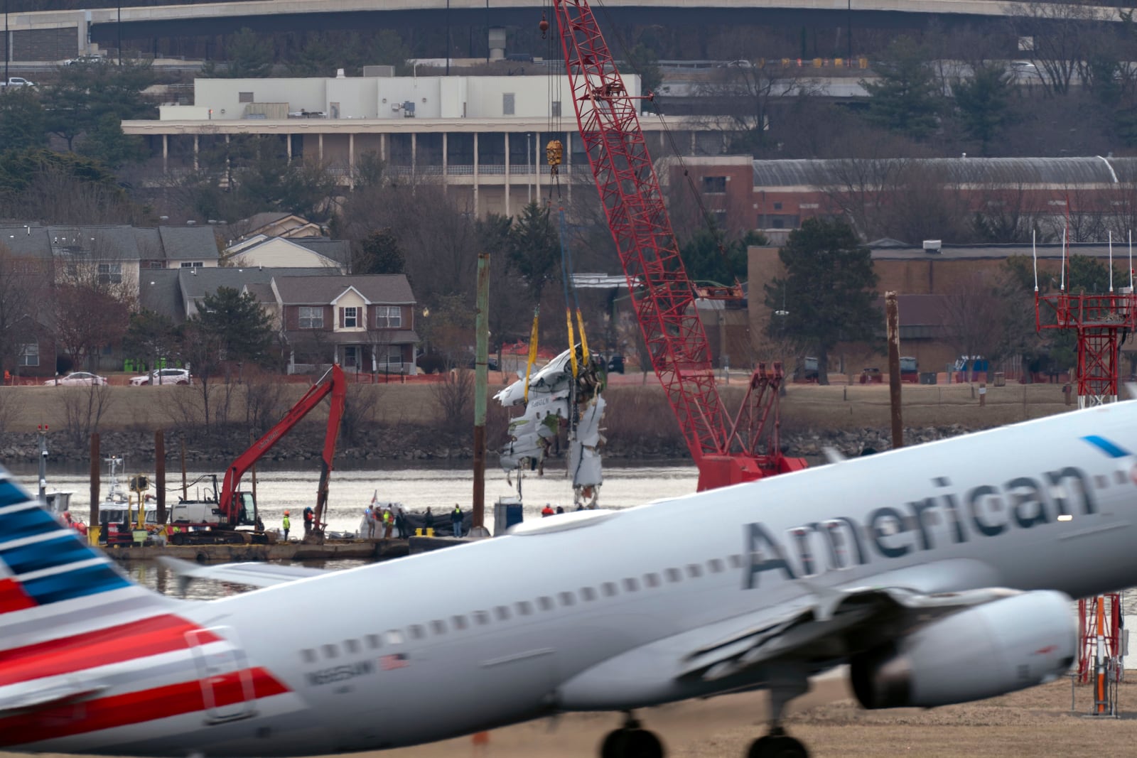 An American Airlines jet passes as rescue and salvage crews with cranes pull up the wreckage of an American Airlines jet in the Potomac River from Ronald Reagan Washington National Airport, Monday, Feb. 3, 2025, in Arlington, Va. (AP Photo/Jose Luis Magana)