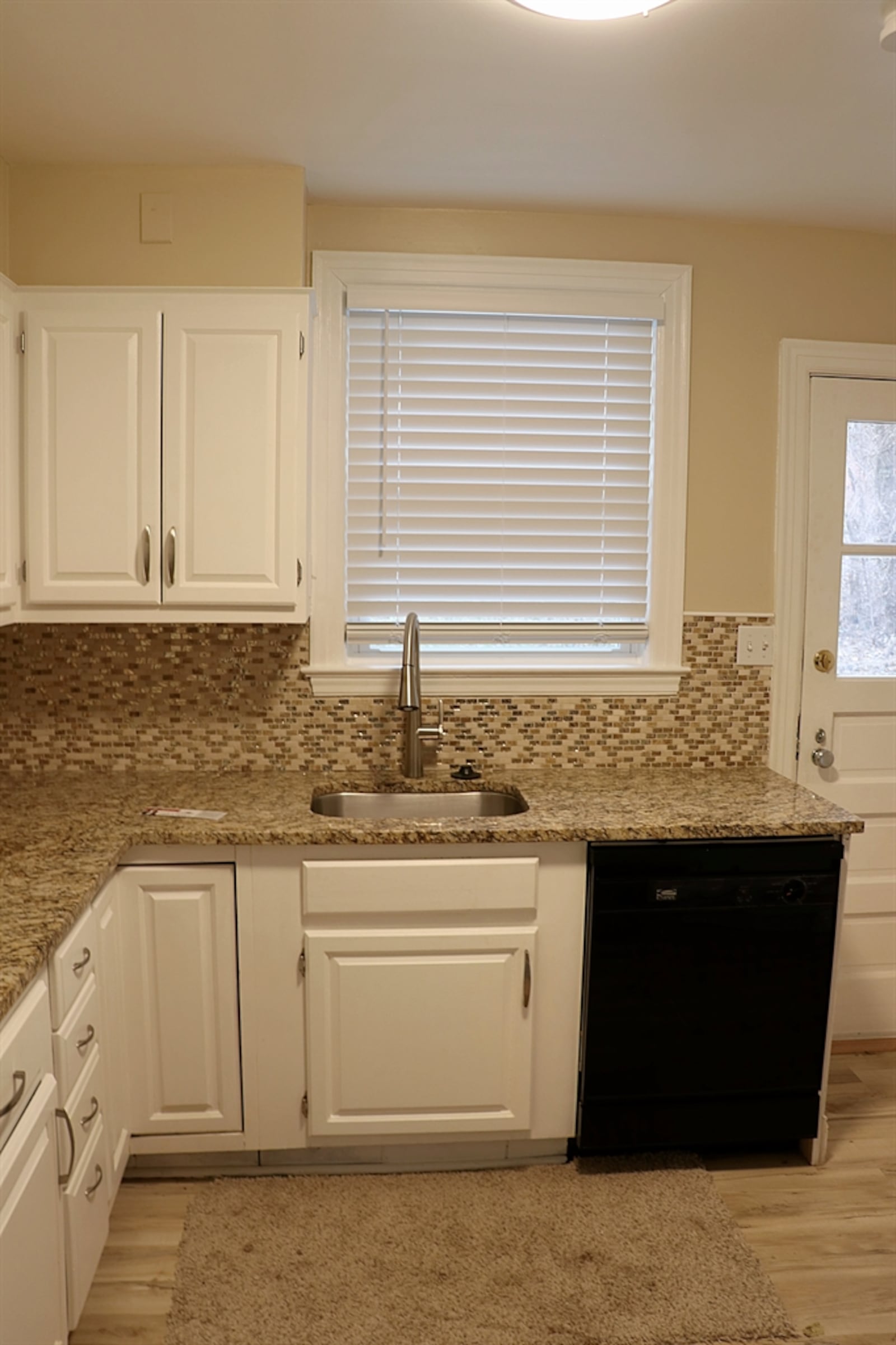 The kitchen has been updated with granite counters that complement the white cabinetry. Mosaic-glass tiles blend from the counter to under the cabinetry, creating a neutral backsplash.