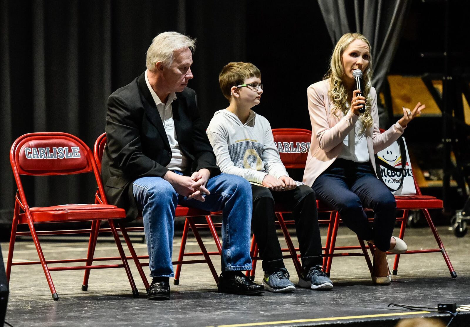 Sarah Curry Rathel speaks about the book “My Cancer Life” starring Matthew Harrison, middle, a sixth-grader at Chamberlain Middle School in Carlisle, during an assembly at the school Friday, Feb. 15. Rathel and illustrator Bob Kelly, left, created the book with proceeds of the book sales will help with treatment costs for Harrison. NICK GRAHAM/STAFF