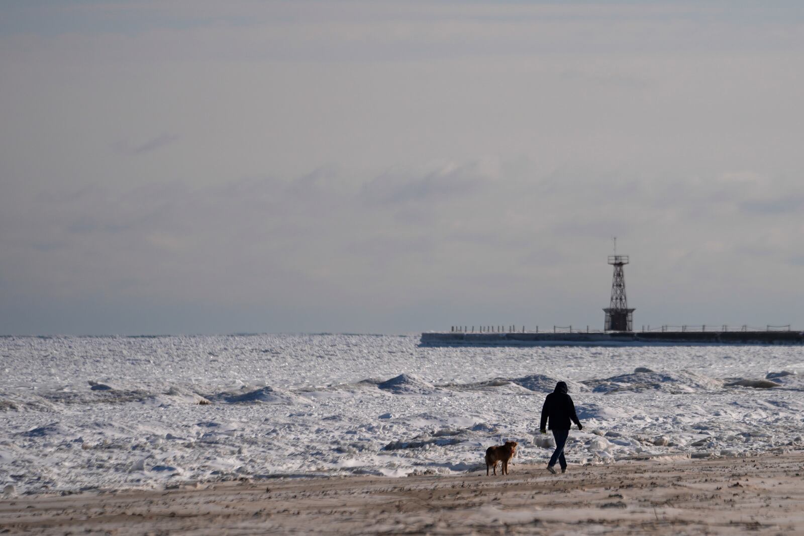 A person walks on a beach along the shore of ice covered Lake Michigan Thursday, Feb. 13, 2025, in Chicago. (AP Photo/Kiichiro Sato)