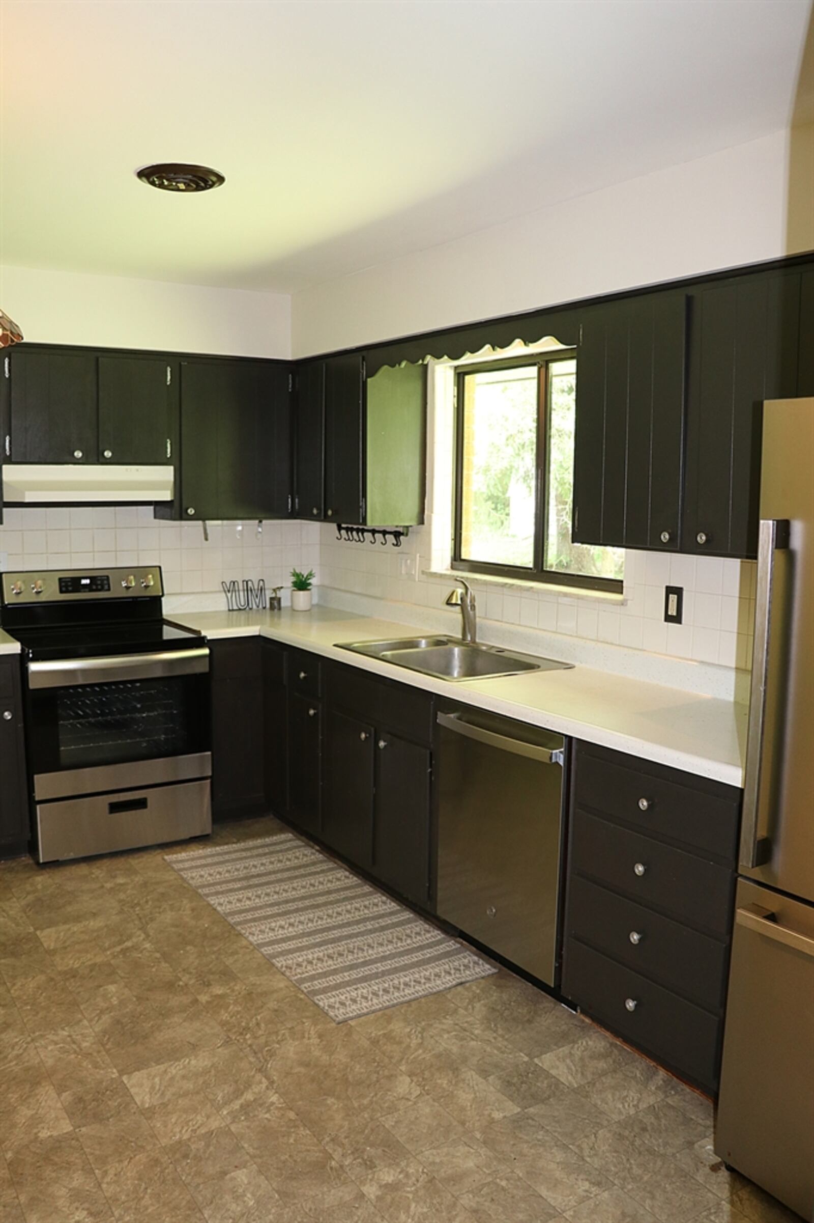 The kitchen has a large sink below a window and painted cabinetry with complementary counters that surround stainless-steel appliances.