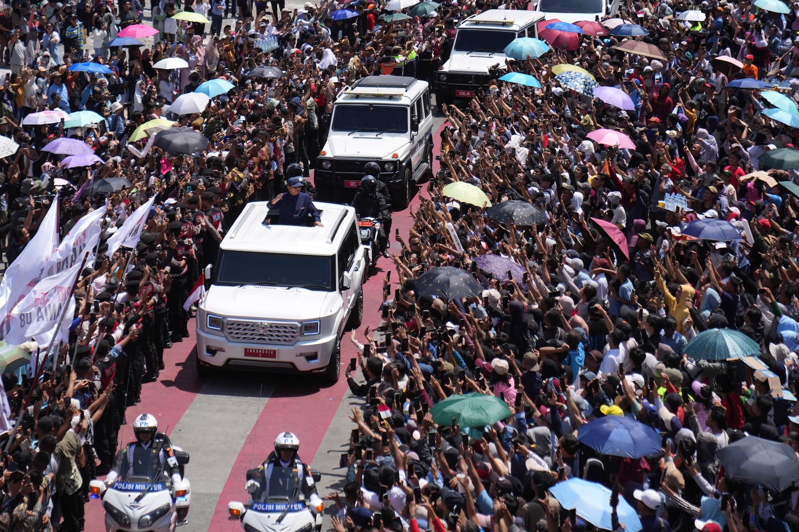 Newly-inaugurated Indonesian President Prabowo Subianto, center left in a vehicle, greets supporters after being sworn in as the country's eighth president in Jakarta, Indonesia, Sunday, Oct. 20, 2024. (AP Photo/Dita Alangkara)