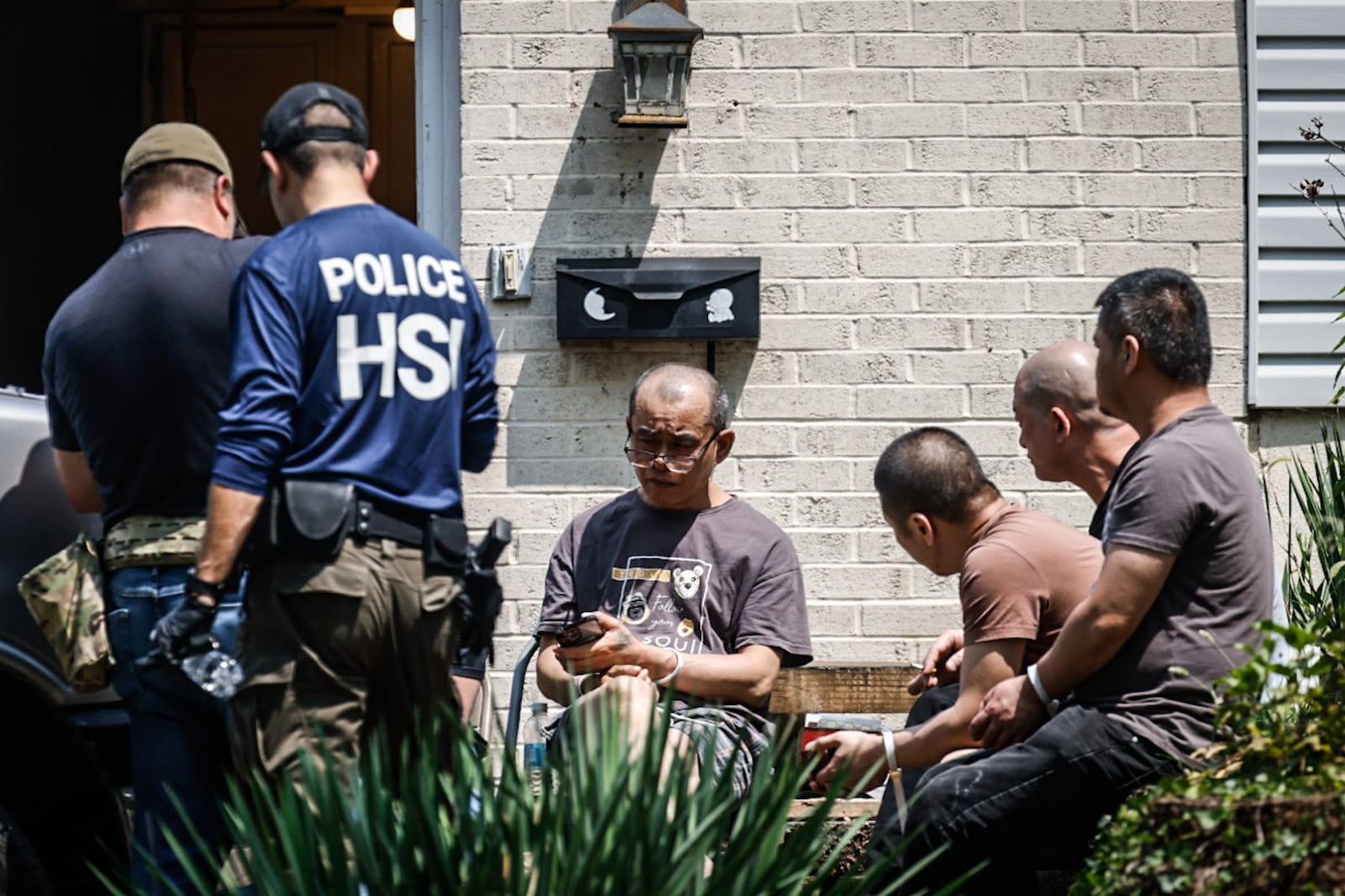 Homeland Security officers and local law enforcement agencies raided a home in the 1100 block of Irving Ave. in Dayton on Friday, July 26. While authorities went in and out of the house, seven people sat outside in zip-tie cuffs. JIM NOELKER / STAFF