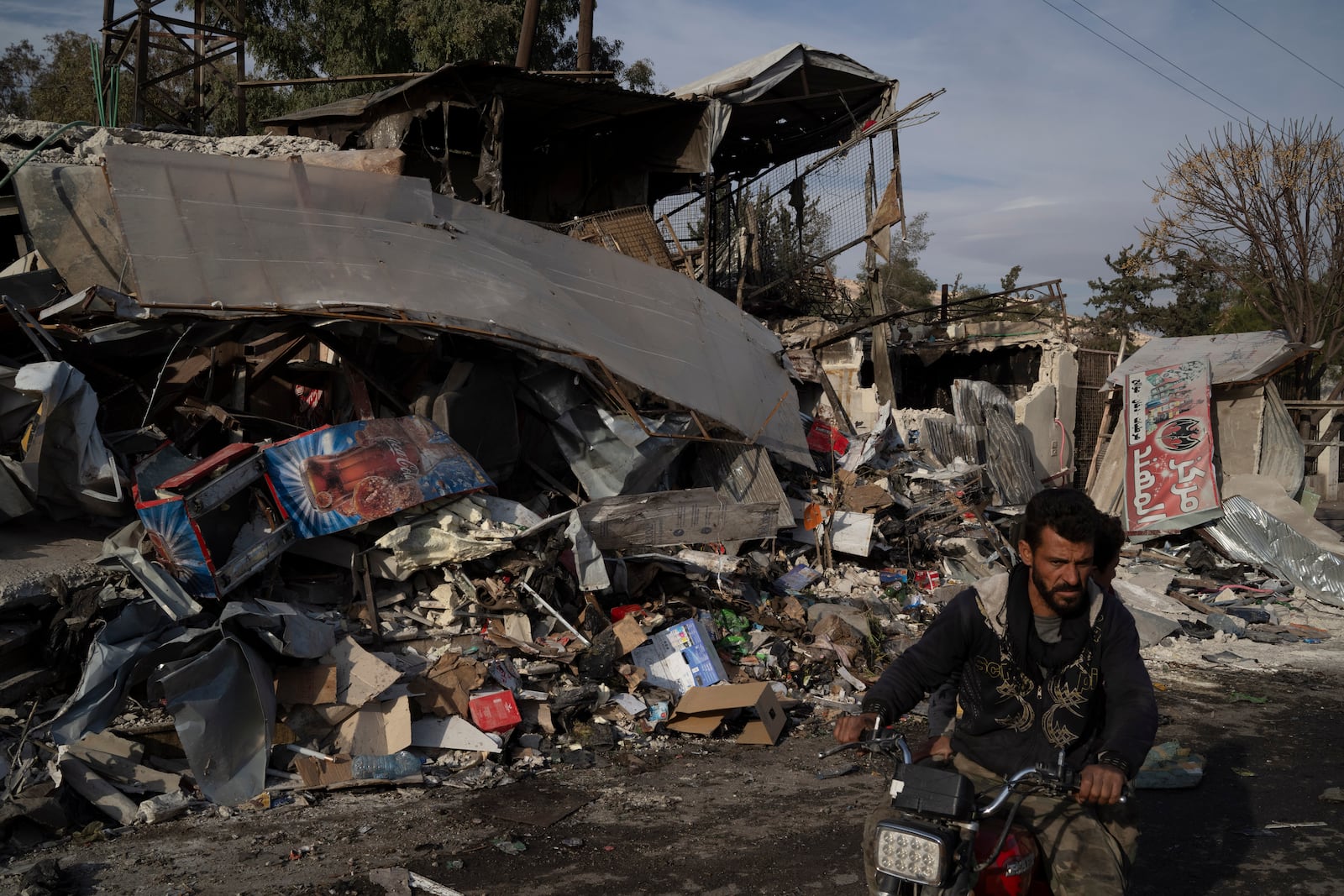 A man rides his motorcycle past shops and stores that, according to locals, have been destroyed for been used or owned by Bashar Assad's supporters, in Damascus, Syria, Thursday, Dec. 12, 2024. (AP Photo/Leo Correa)