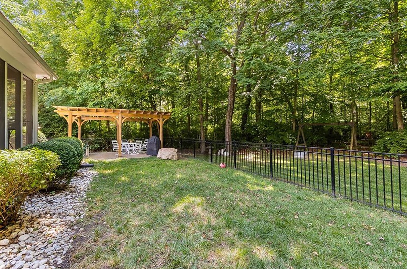 The back yard is partially fenced with metal fencing and has a firepit and woods beyond the fence.