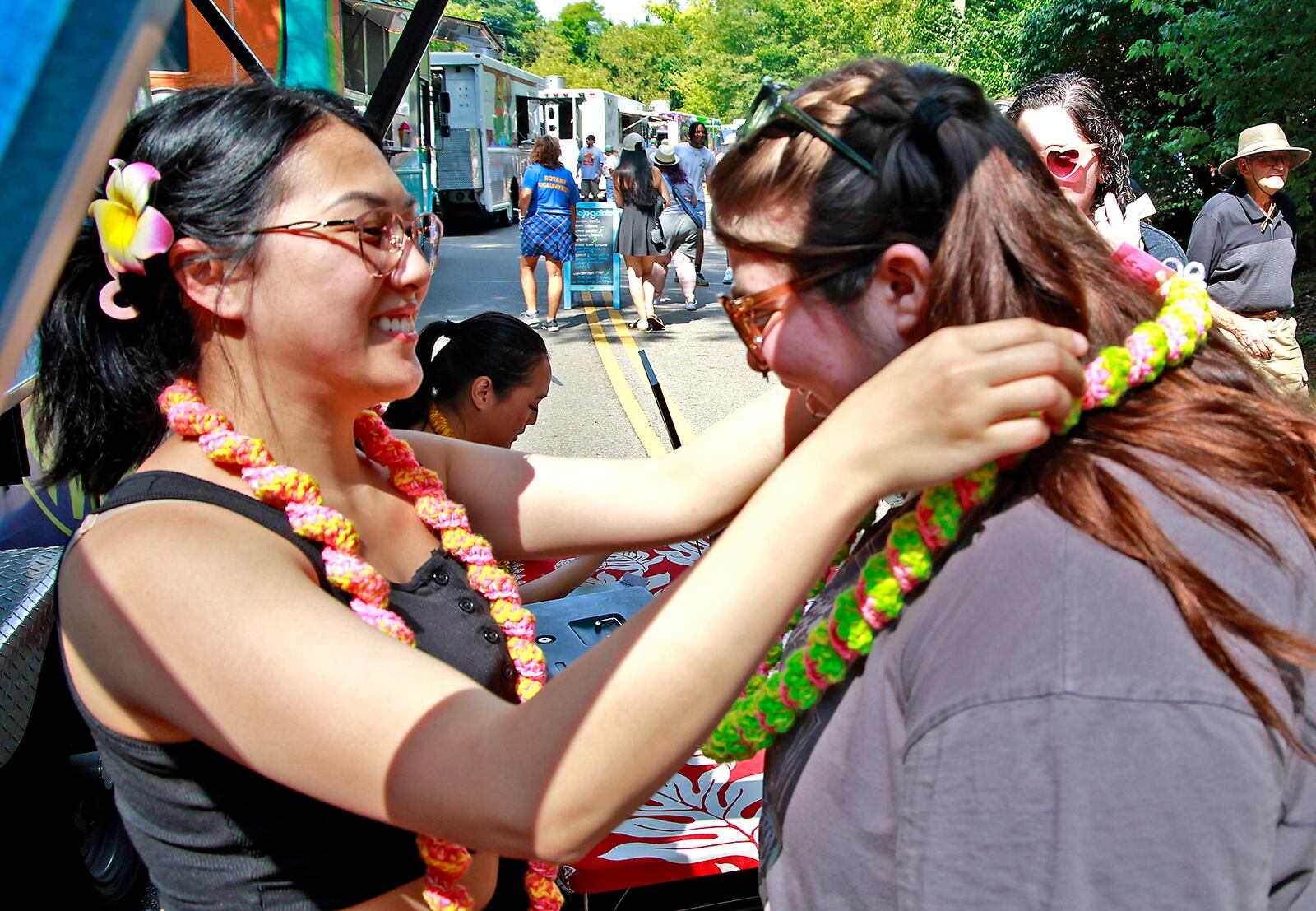 Praewa Wu, from the Dine-In Hawaiian food truck, places a Hawaiian lei around Pyper Frizzell's neck Saturday, August 17, 2024 at the 10th annual Springfield Rotary Gourmet Food Truck Competition in Veterans Park. BILL LACKEY/STAFF