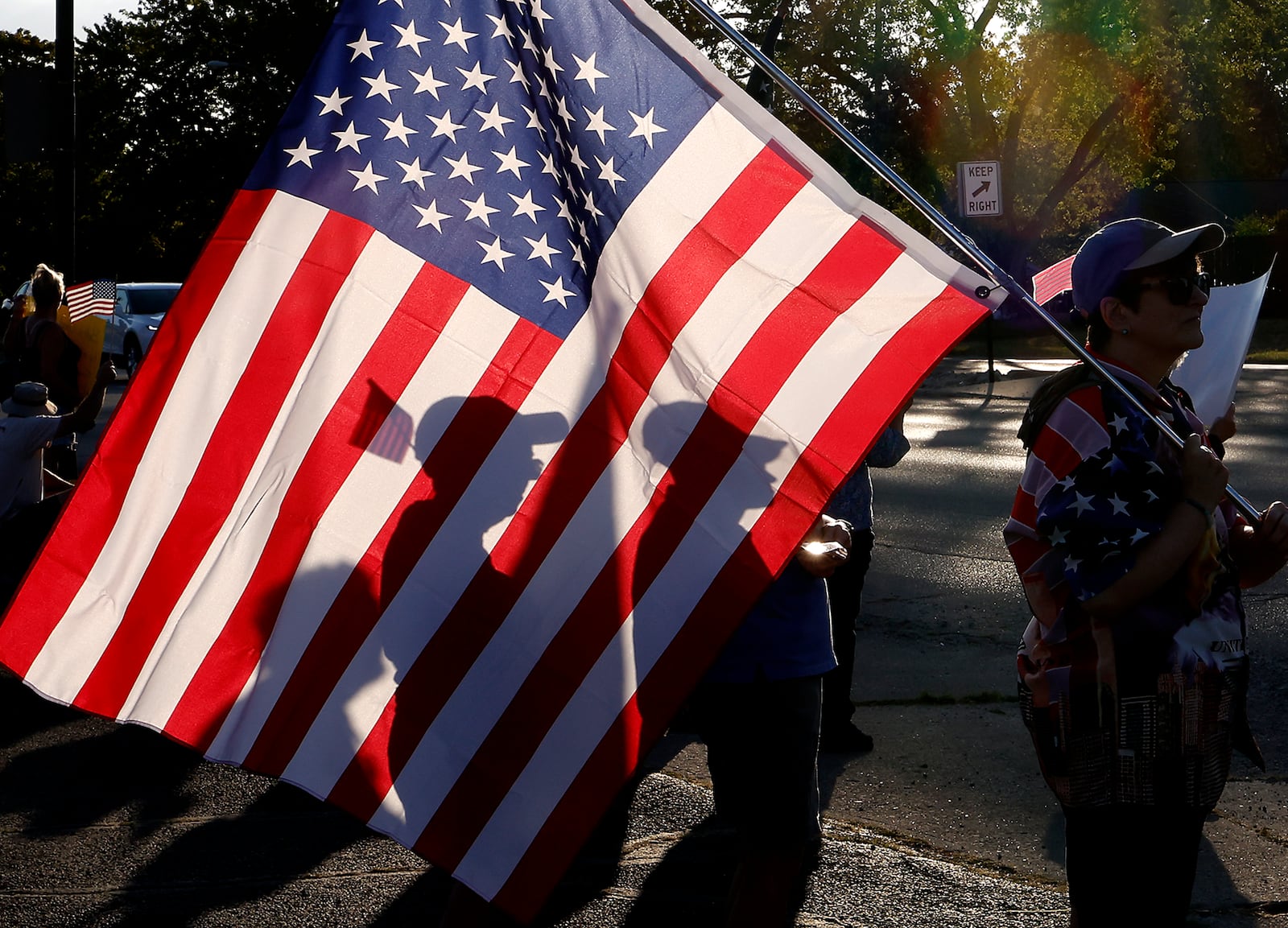 Three participants in Wednesday evening's Peace Rally at the Springfield Democratic Headquarters are silhouetted through an American flag as the sun sets along Park Road. BILL LACKEY/STAFF