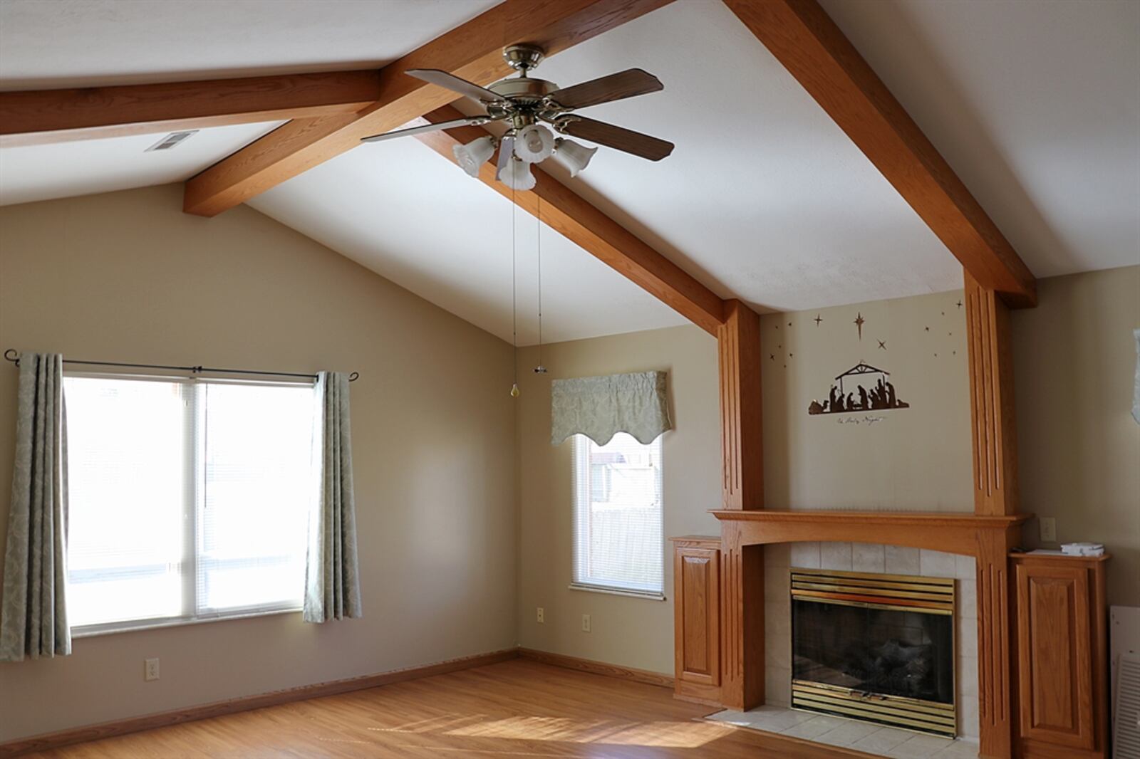 A cathedral ceiling expands the great room off the kitchen and oak beams cross the ceiling and extend down to the fireplace mantel, bringing the gas fireplace into the design focus. The oak beams cross the ceiling and meet at the peak. The lower beams connect to the gas fireplace mantel that has built-in media cabinets flanking the firebox.