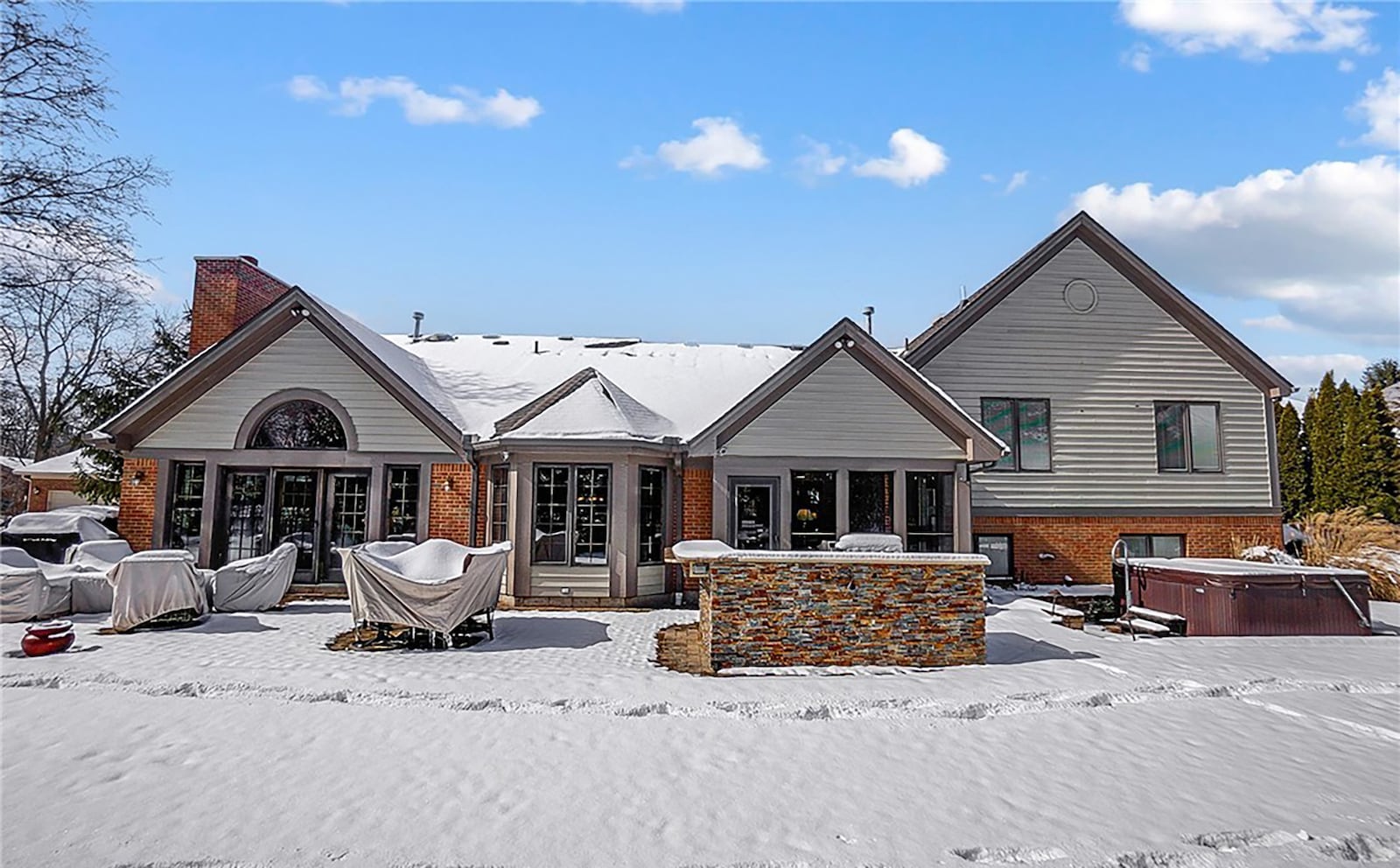 The rear of the home has a concrete patio with an outdoor kitchen area and hot tub with surrounding brick wall.