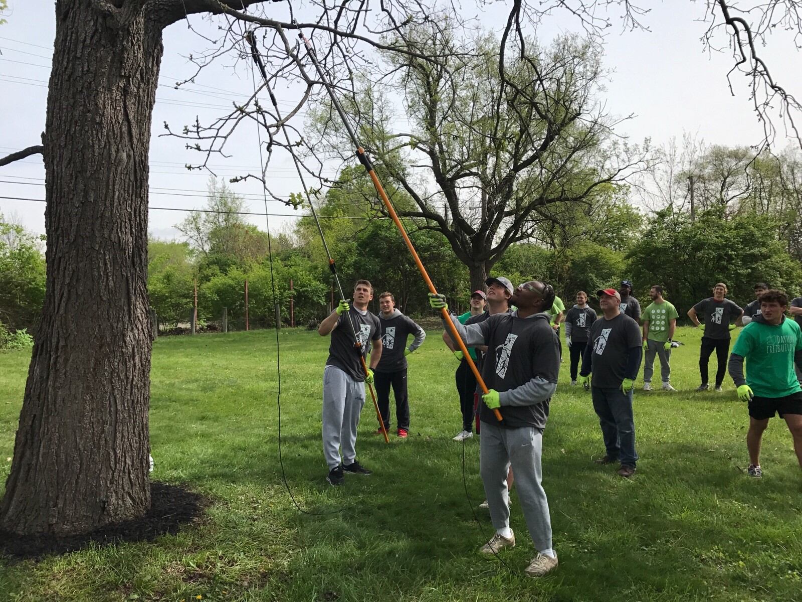 UD football players trim branches on Charles Harden’s property as Flyers head coach Trevor Andrews (red and white cap, dark shirt) looks on. Tom Archdeacon/CONTRIBUTED