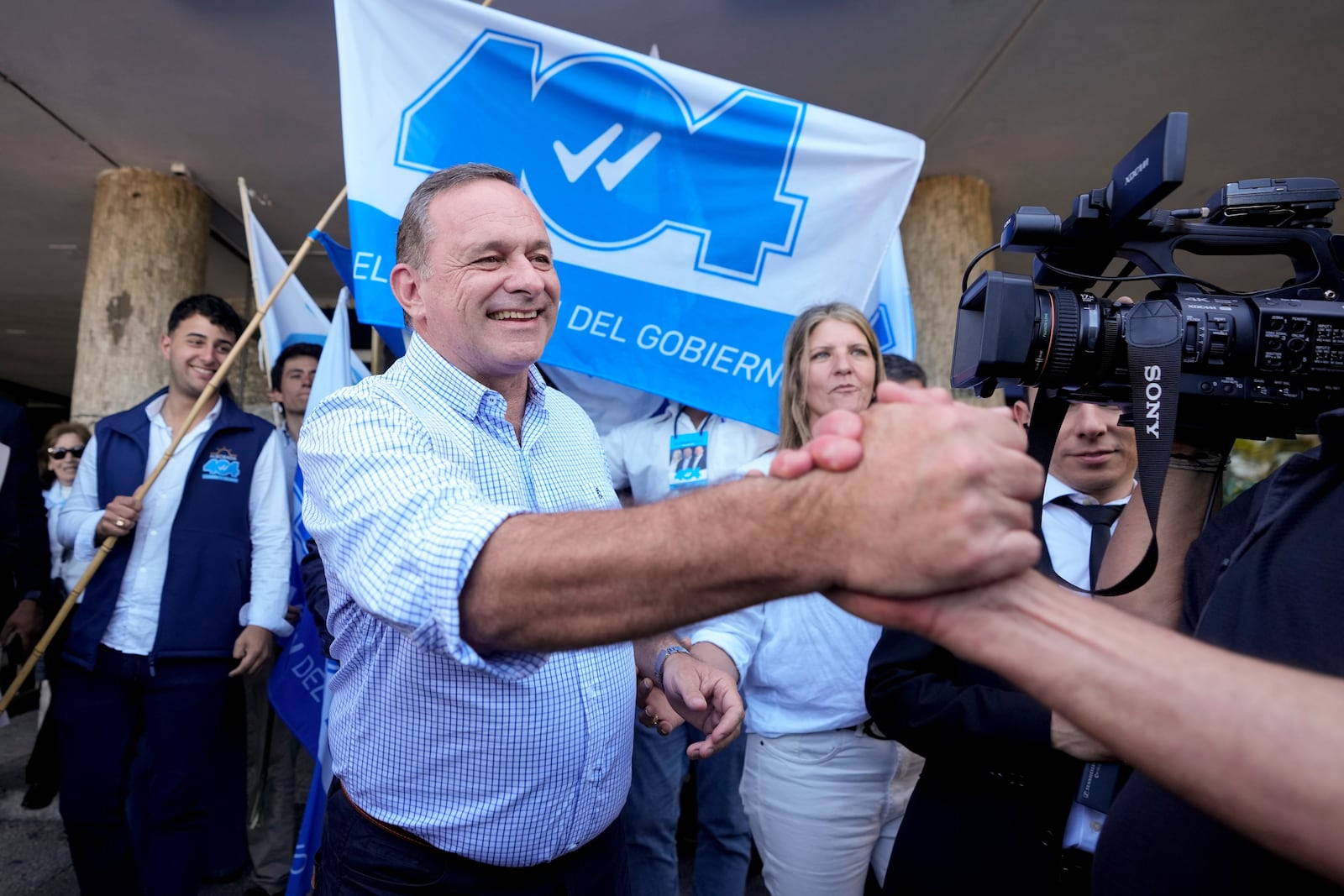 Alvaro Delgado, presidential candidate for the ruling National Party, center, greets a supporter outside a polling station during general elections in Montevideo, Uruguay, Sunday, Oct. 27, 2024. (AP Photo/Natacha Pisarenko)