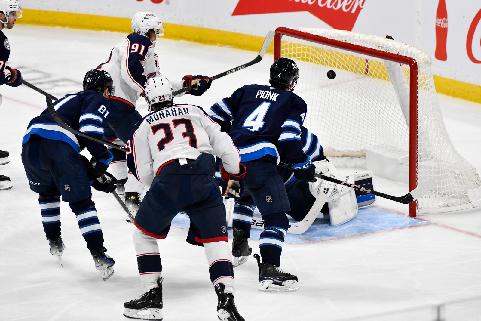 Columbus Blue Jackets' Kent Johnson (91) scores against Winnipeg Jets' goaltender Eric Comrie, back right, during third-period NHL hockey game action in Winnipeg, Manitoba, Sunday Dec. 8, 2024. (Fred Greenslade/The Canadian Press via AP)