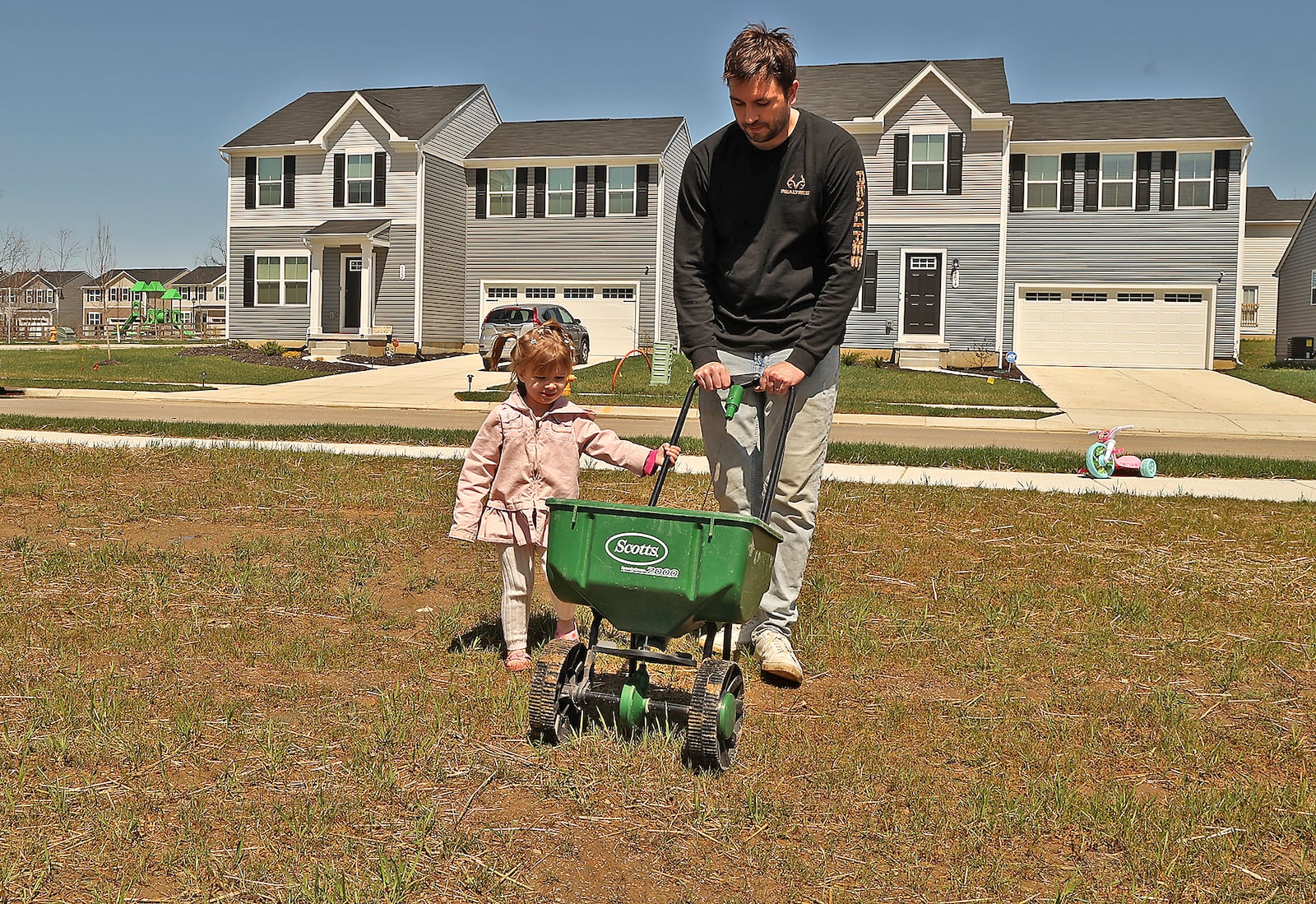 Riley Goss, 2, helps her father, Nick, sew grass seed in their new yard in the Bridgewater development. BILL LACKEY/STAFF