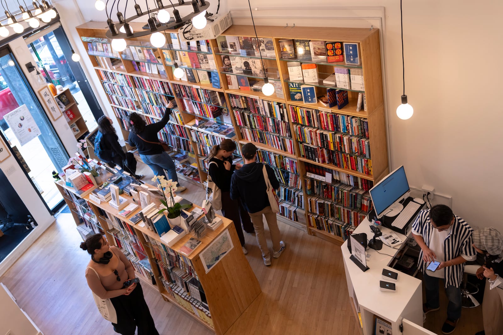 Yu Miao, right, owner of JF Books, looks at his phone as customers browse the books in his bookstore in Washington, Thursday, Oct. 3, 2024. (AP Photo/Ben Curtis)