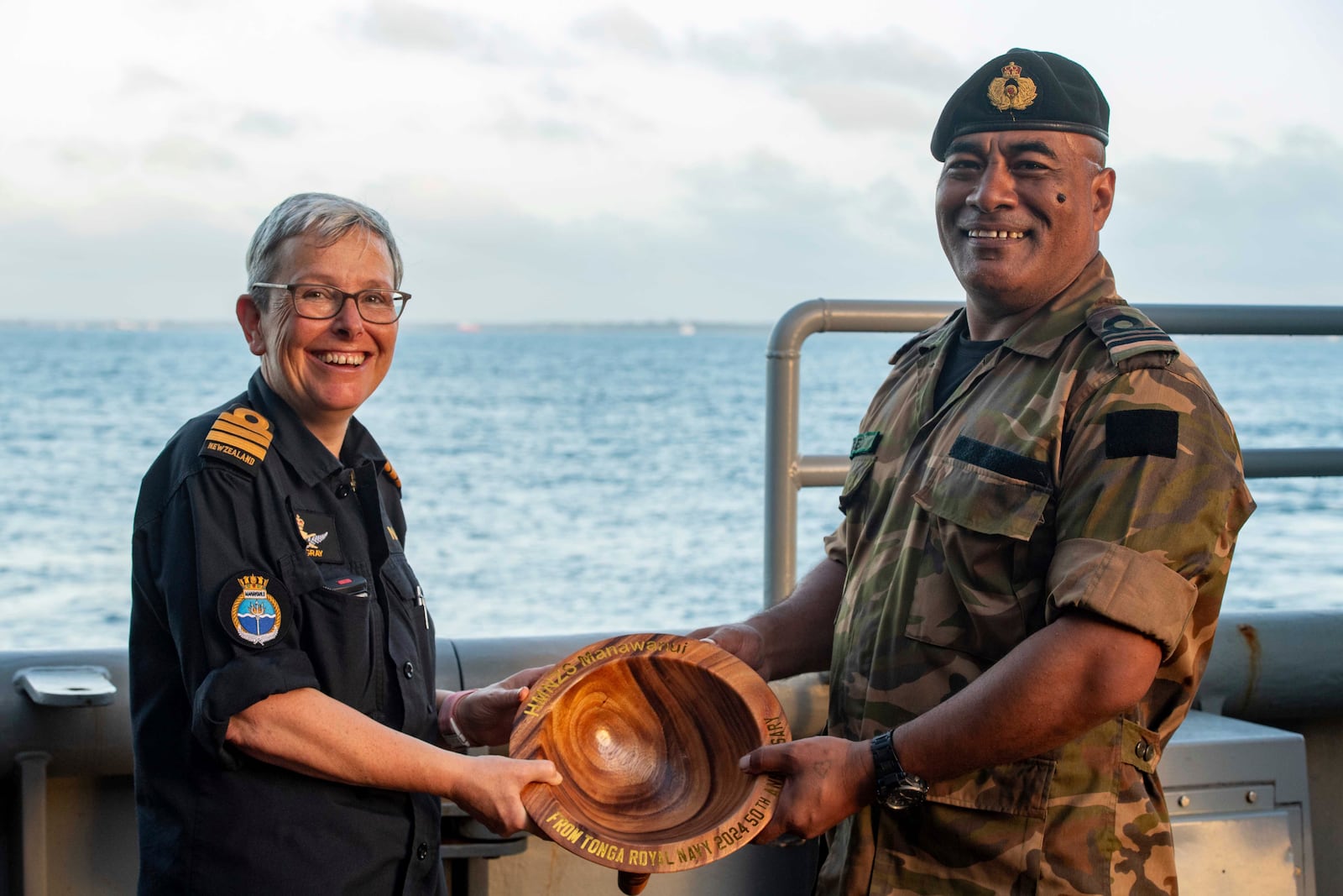 In this undated photo provided by the New Zealand Defence Force, Lieutenant Commander Tala Mafile'o of the Royal Tongan Navy presents Commander Yvonne Gray, left, with a carved wooden bowl as a memento of the RNZN's participation in the 50th Anniversary Fleet Review. (New Zealand Defence Force via AP)