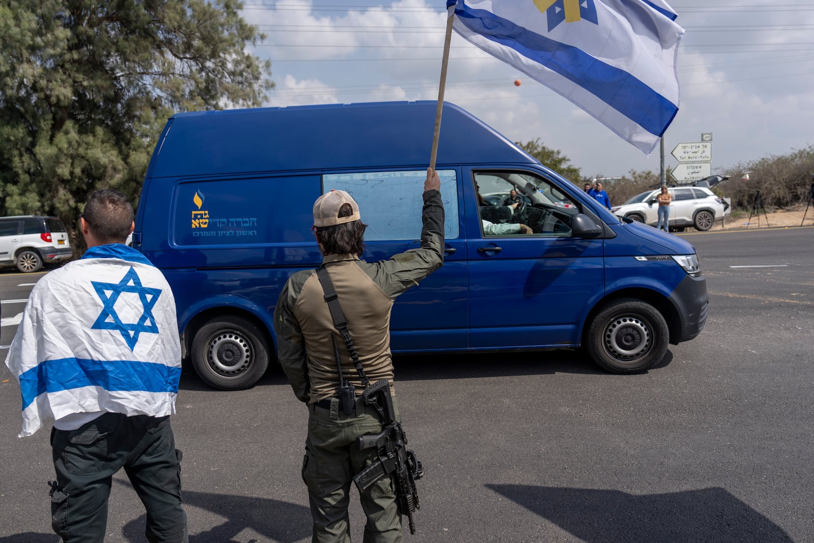 Israelis wave flags as the car carrying the coffin of slain Israeli hostage Ohad Yahalomi, passes by during his funeral procession in Kibbutz Nir Oz, southern Israel, Wednesday, March 5, 2025. (AP Photo/Ariel Schalit)