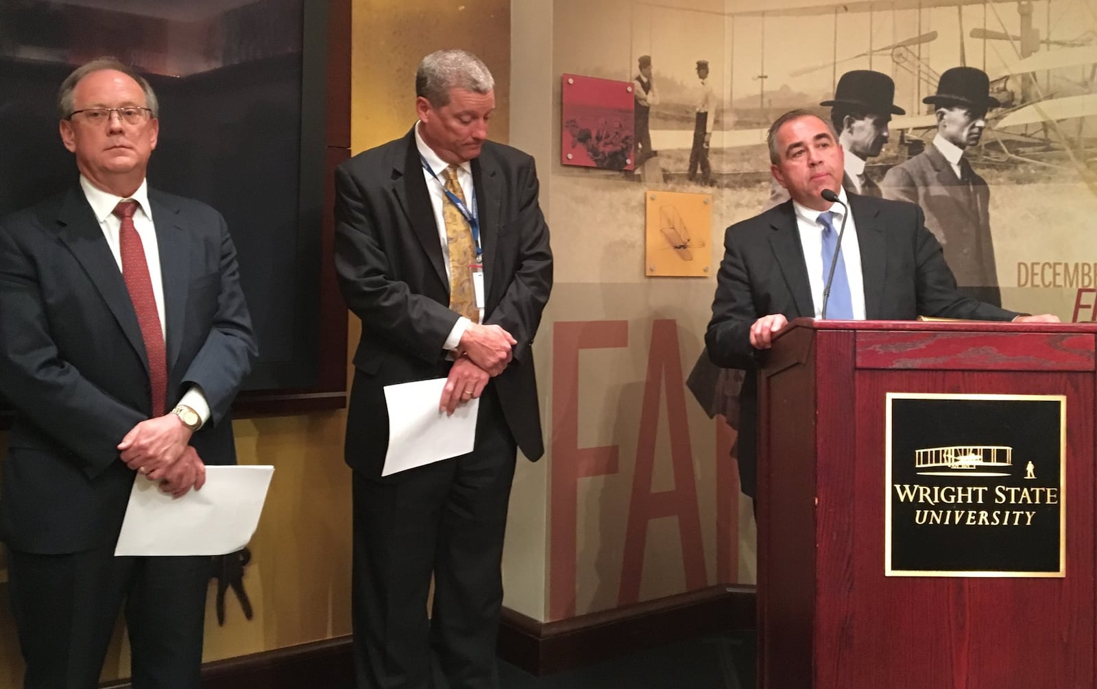 Wright State University officials speak at a press conference following the release of a controversial audit report. Dennis Andersh, executive director of the Wright State Research Institute, stands to the far left of the podium next to Doug Fecher, vice chairman of the WSU board of trustees. Michael Bridges, chairman of the board, speaks about the audit.