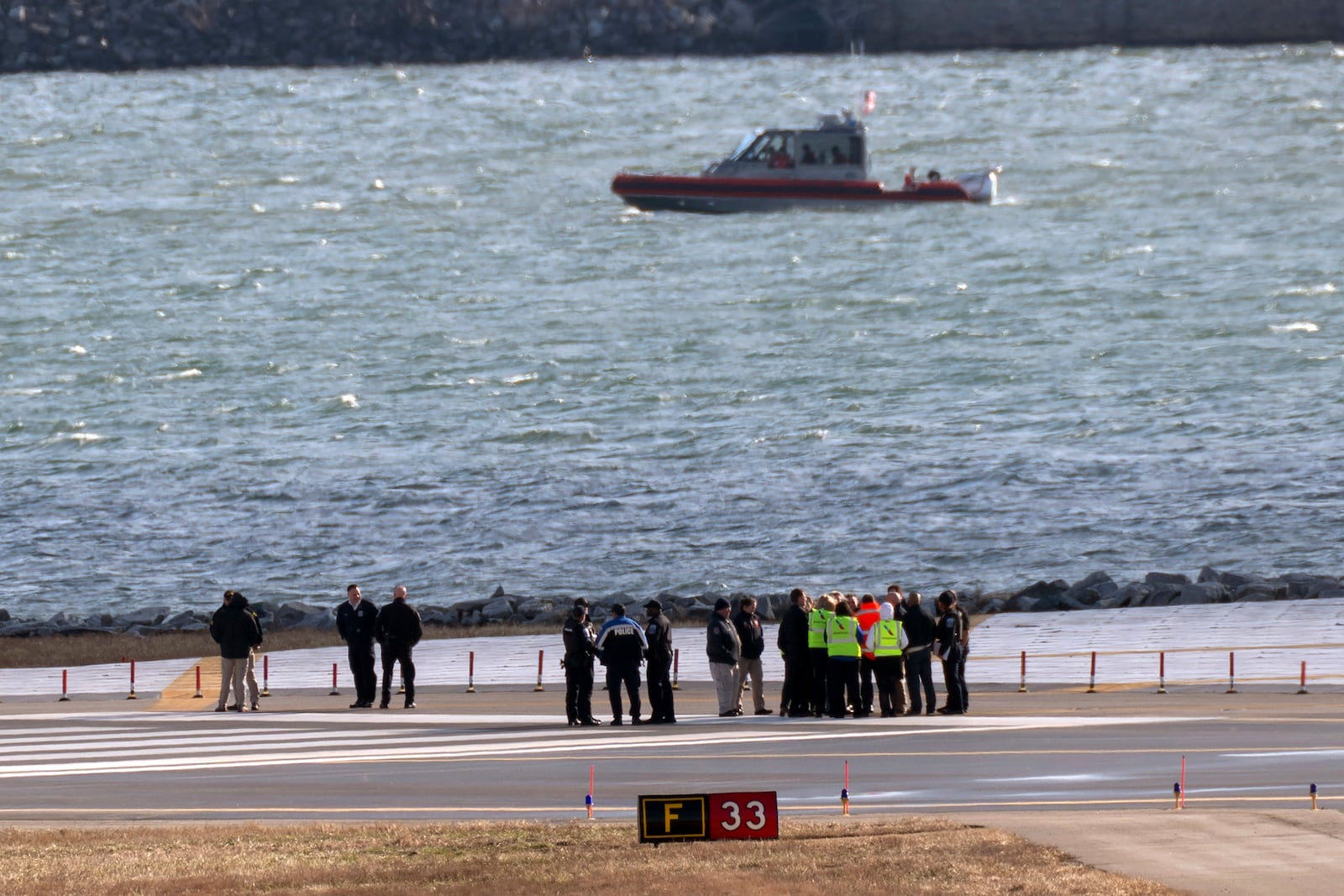 Officials gather at the end of runway 33 near the wreckage site in the Potomac River of a mid-air collision between an American Airlines jet and a Black Hawk helicopter at Ronald Reagan Washington National Airport, Saturday, Feb. 1, 2025, in Arlington, Va. (AP Photo/Jose Luis Magana)