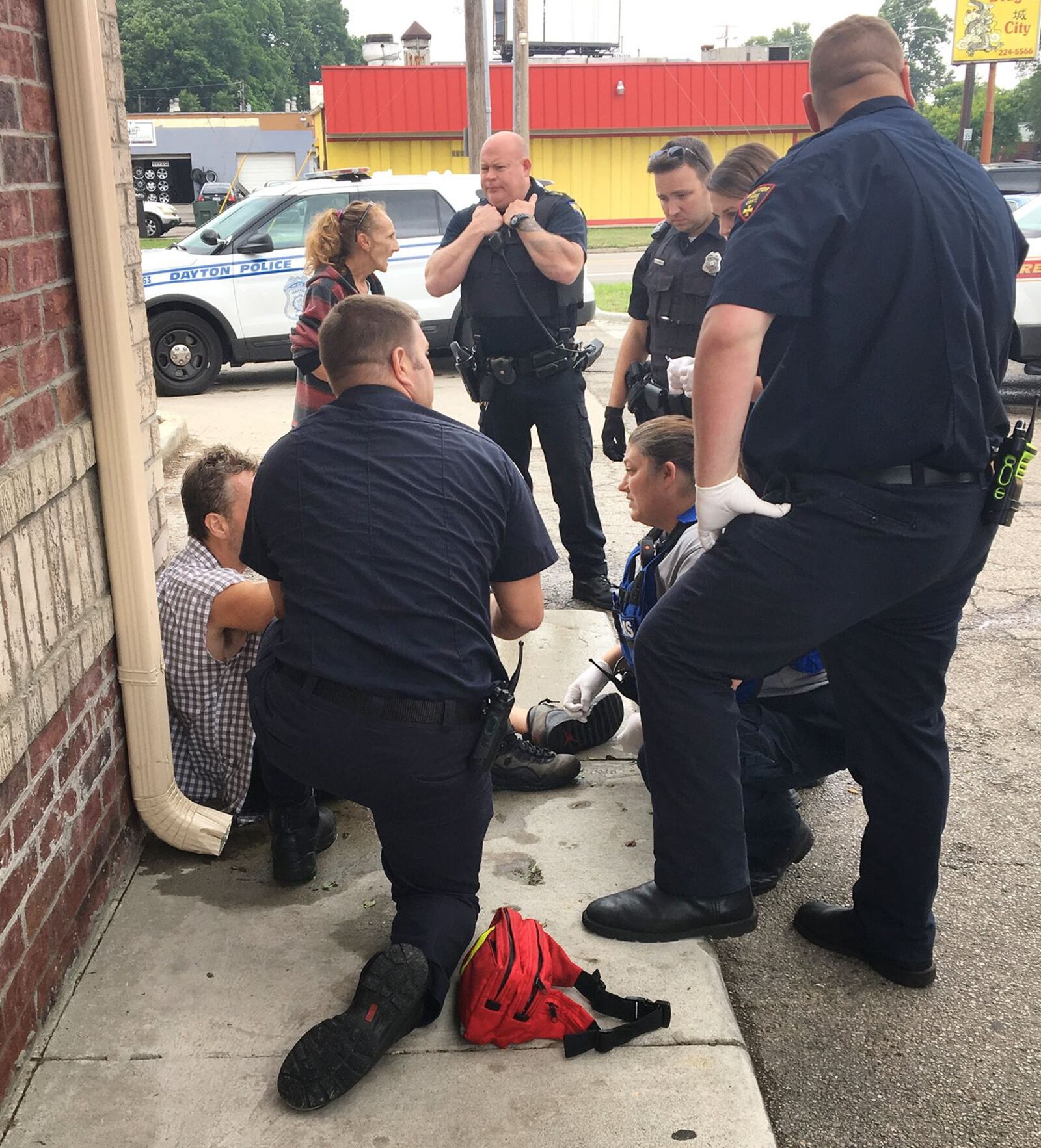 Dayton EMT Amy Dunkin, kneeling, and other first responders talk with a man who was just revived from an heroin overdose at a gas station on Keowee Street. KATIE WEDELL/STAFF