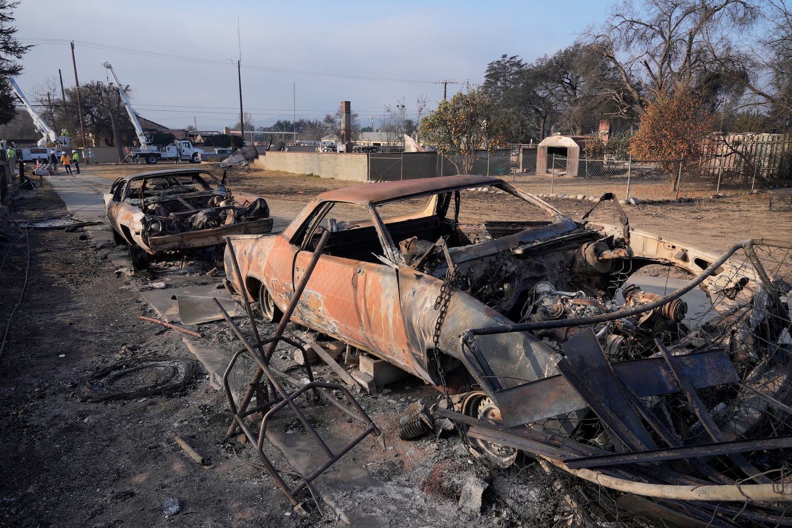 Southern California Edison utility company workers in rear try to restore power in the area destroyed by the Eaton Fire, Sunday, Jan. 19, 2025, in Altadena, Calif. (AP Photo/Damian Dovarganes)