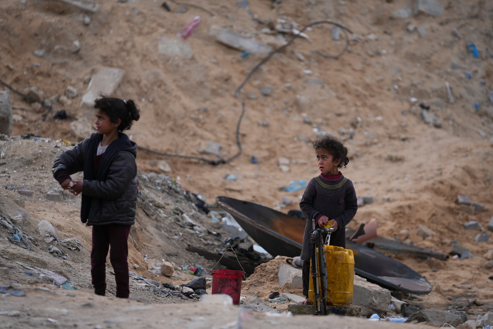 Displaced Palestinians girls fill a plastic jerrycan with water at a school run by UNRWA, the U.N. agency helping Palestinian refugees, which they use as a shelter west of Gaza City, Sunday, March 9, 2025. (AP Photo/Jehad Alshrafi)