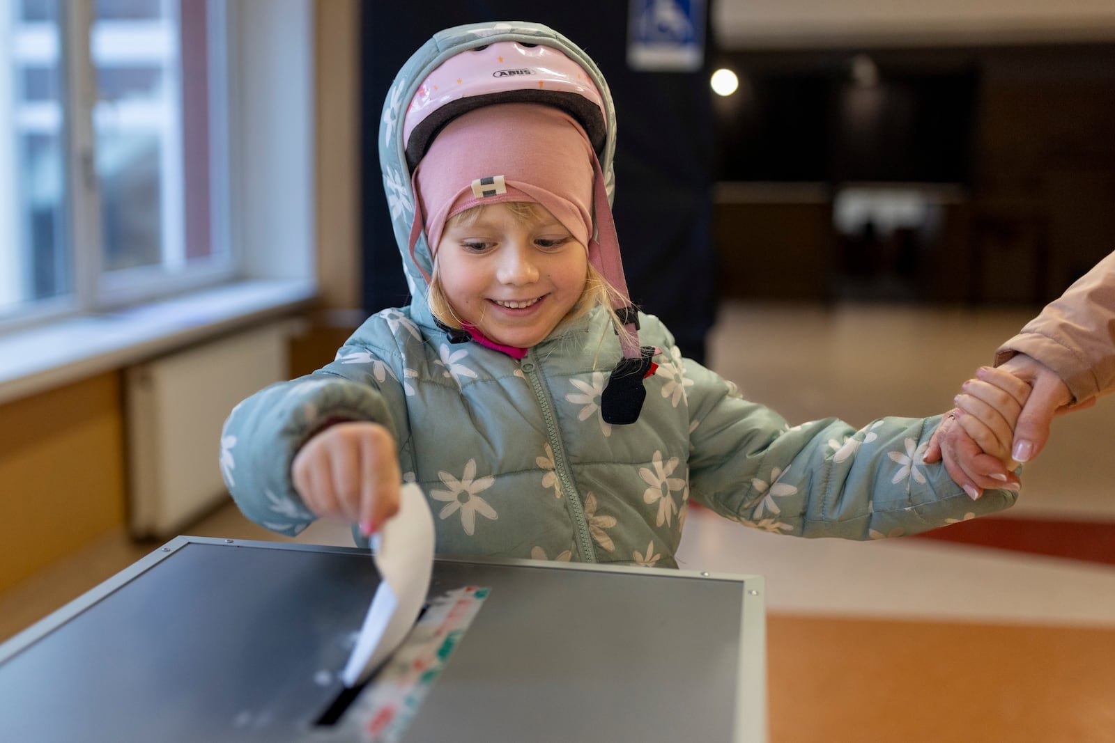 A girl helps to cast a ballot at a polling station during a second round of voting in parliamentary election, in Vilnius, Lithuania, Sunday, Oct. 27, 2024. (AP Photo/Mindaugas Kulbis)