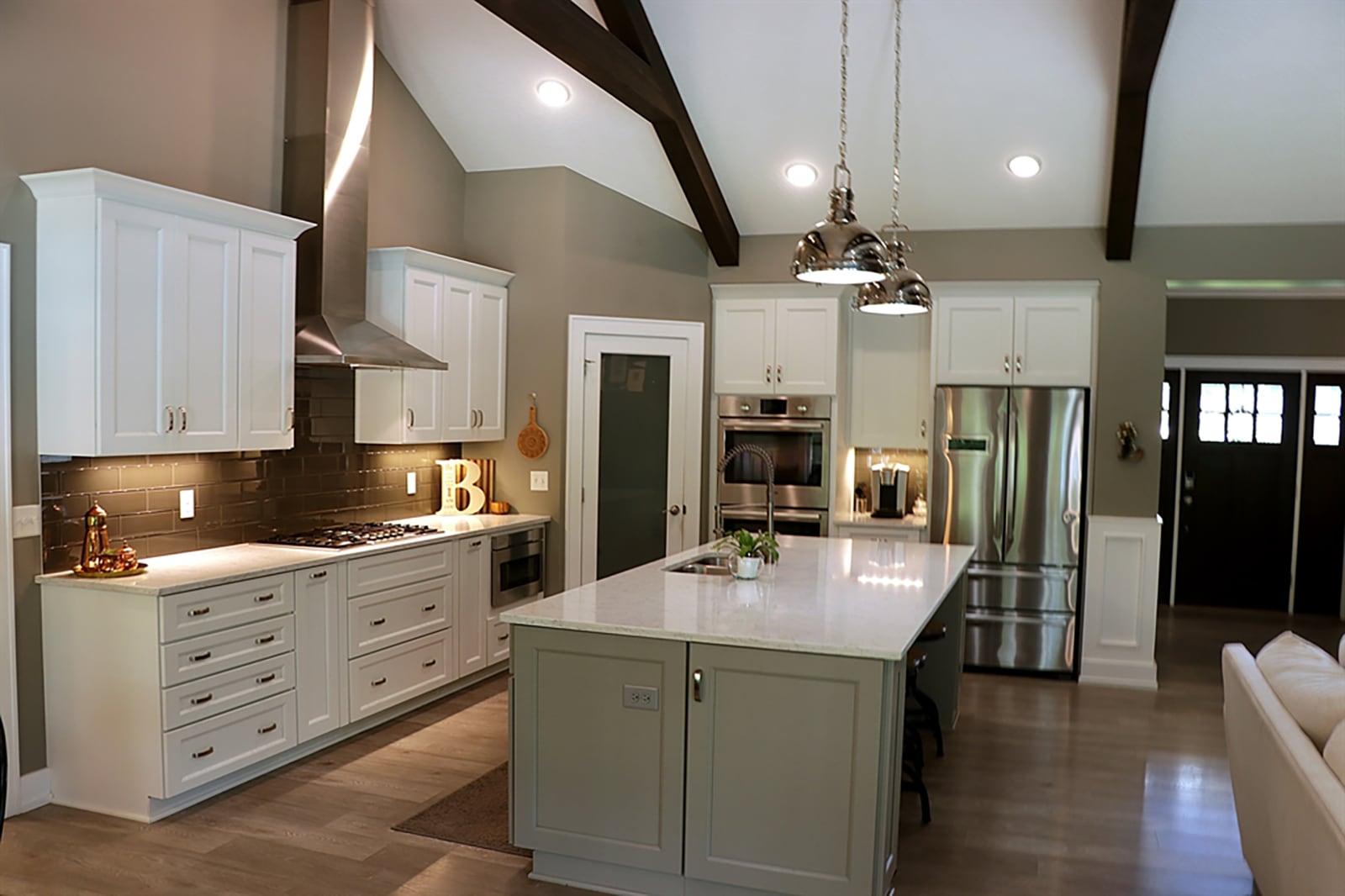 An island offers breakfast bar seating for up to four within the great room side, while on the kitchen side, the island includes a double sink and dishwasher within a quartz countertop. White cabinetry is accented by subway, glass-tile backsplash. CONTRIBUTED PHOTO BY KATHY TYLER