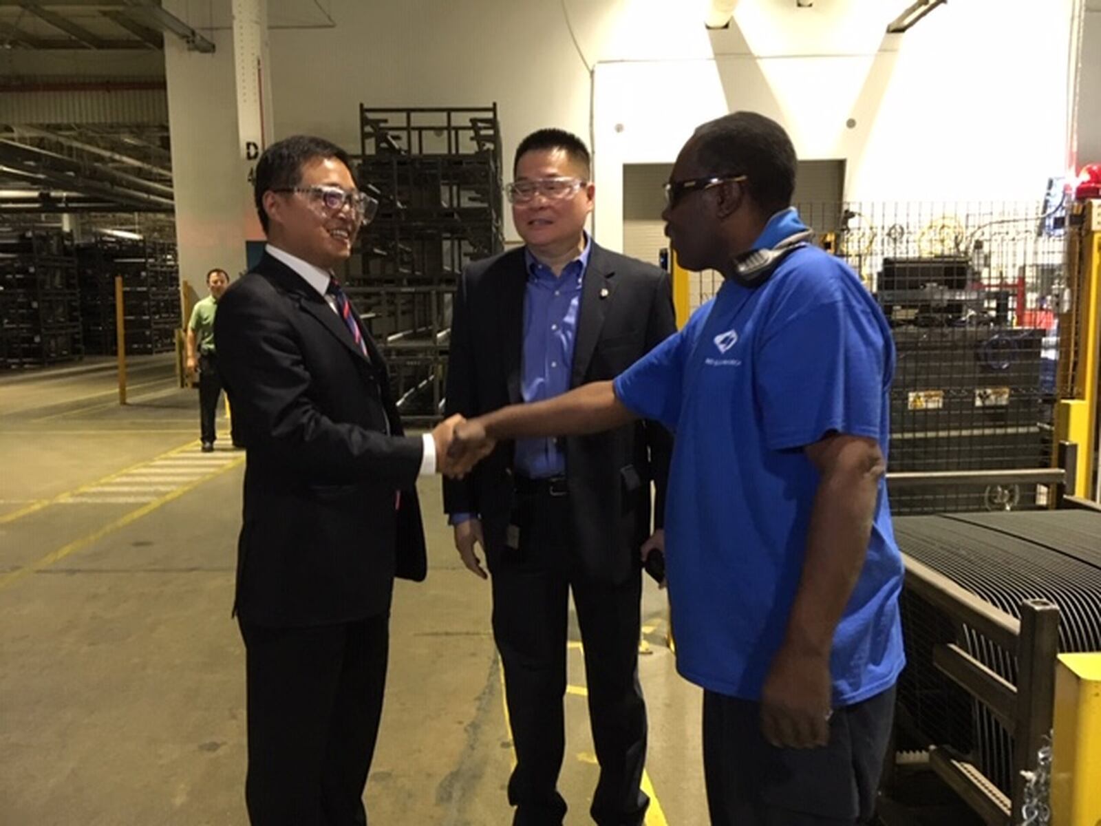 From left, Jin Qian, deputy consul general for the Chinese Consulate in New York, with Jeff Liu, president of Fuyao Glass America, greet a Fuyao worker during a tour of the Fuyao plant in Moraine Wednesday. THOMAS GNAU/STAFF