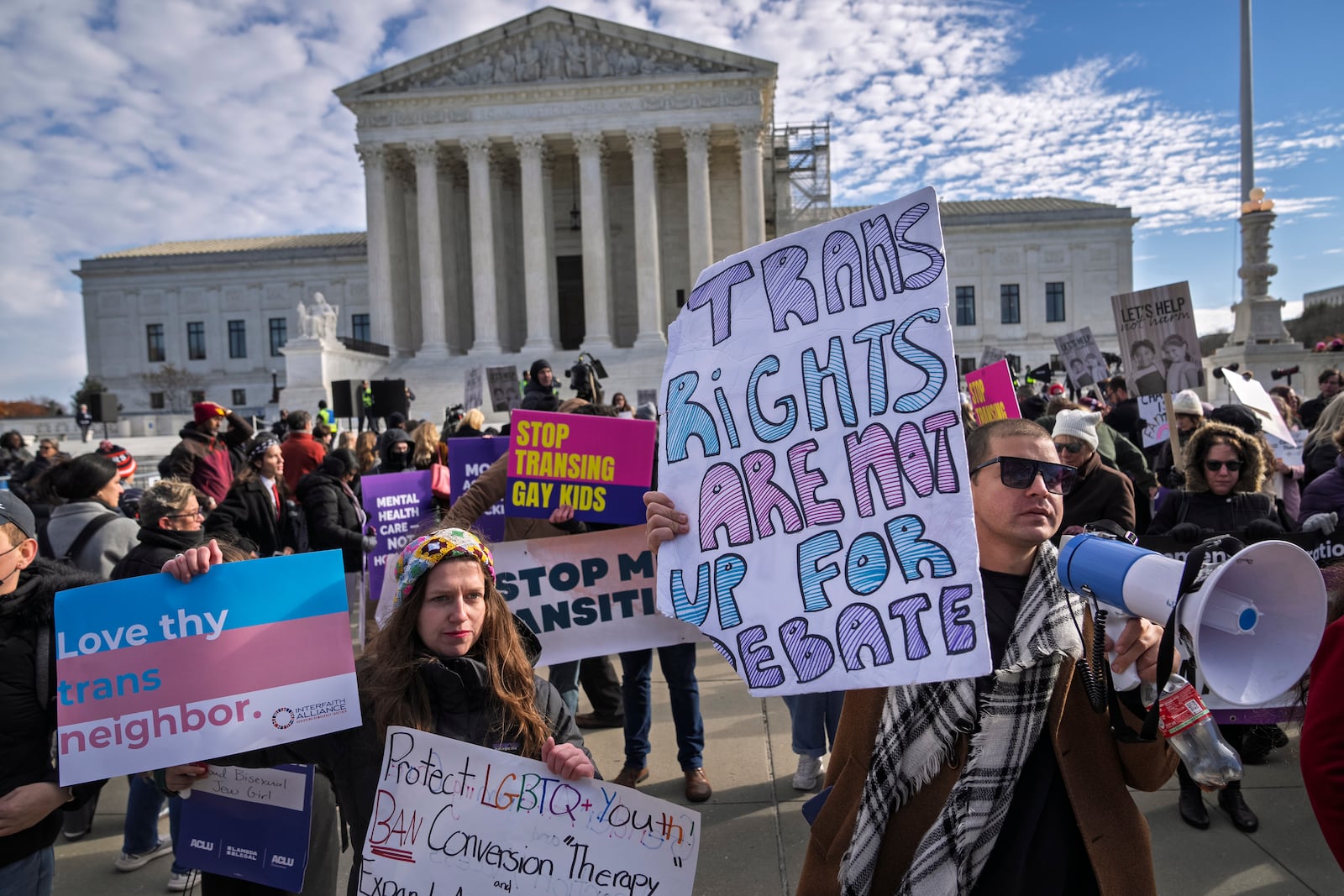 Supporters of transgender rights Sarah Kolick, left, of Cleveland, and Derek Torstenson, of Colorado Springs, Colo., right, rally by the Supreme Court, Wednesday, Dec. 4, 2024, in Washington, while arguments are underway in a case regarding a Tennessee law banning gender-affirming medical care for transgender youth. Behind the two are people who support the ban. (AP Photo/Jacquelyn Martin)