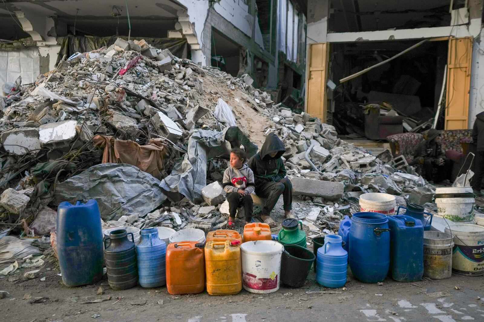 Two children wait to get water next to a line of empty jerrycans in an area largely destroyed by the Israeli army's air and ground offensive in Gaza City, Gaza Strip, Wednesday, Feb. 5, 2025. (AP Photo/Abdel Kareem Hana)