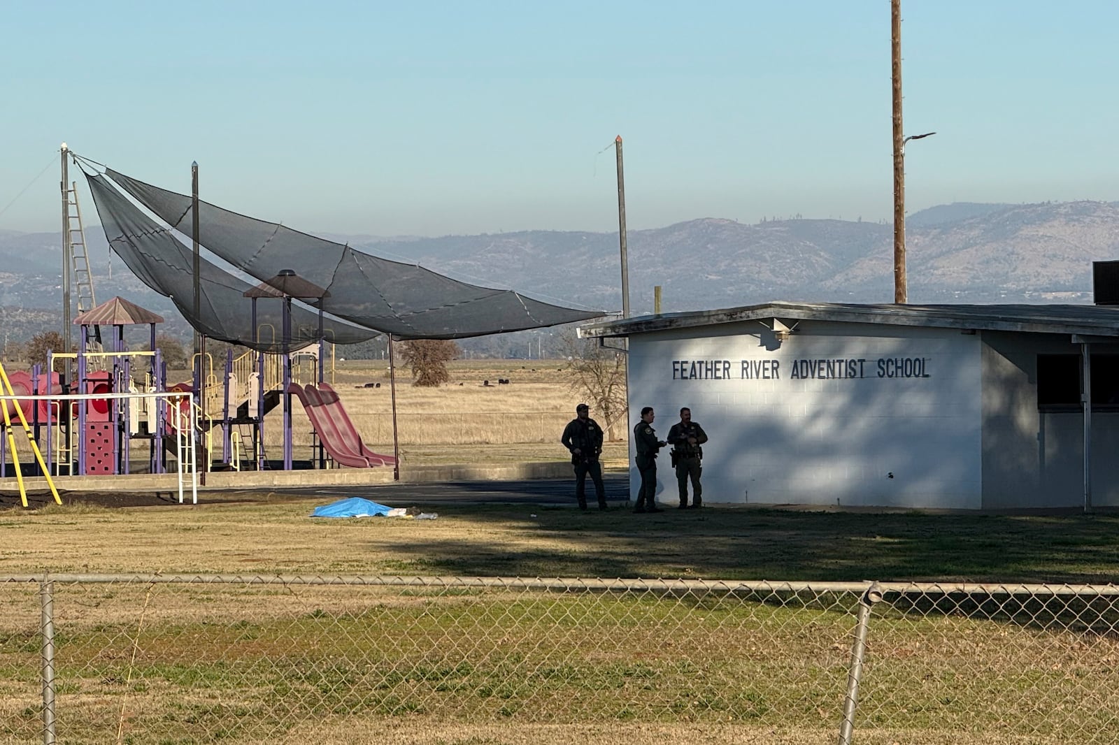 Police officers stand near a body covered by a tarp outside of Feather River Adventist School after a shooting Wednesday, Dec. 4, 2024, in Oroville, Calif. (Michael Weber/The Chico Enterprise-Record via AP)