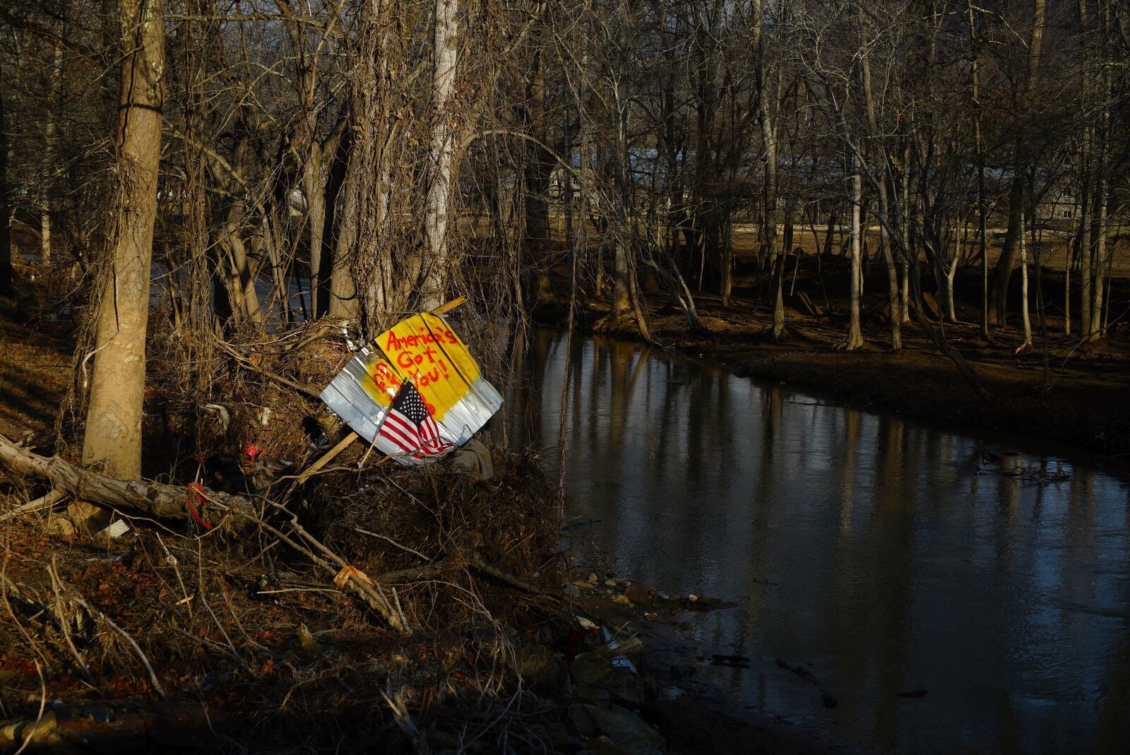 A piece of debris with an American flag and inspirational message stand along a riverbank in Swannanoa, N.C., on Friday, Feb. 7, 2025. More than four months after the remnants of Hurricane Helene devastated western North Carolina, many residents are frustrated with the federal response. (AP Photo/Allen G. Breed)