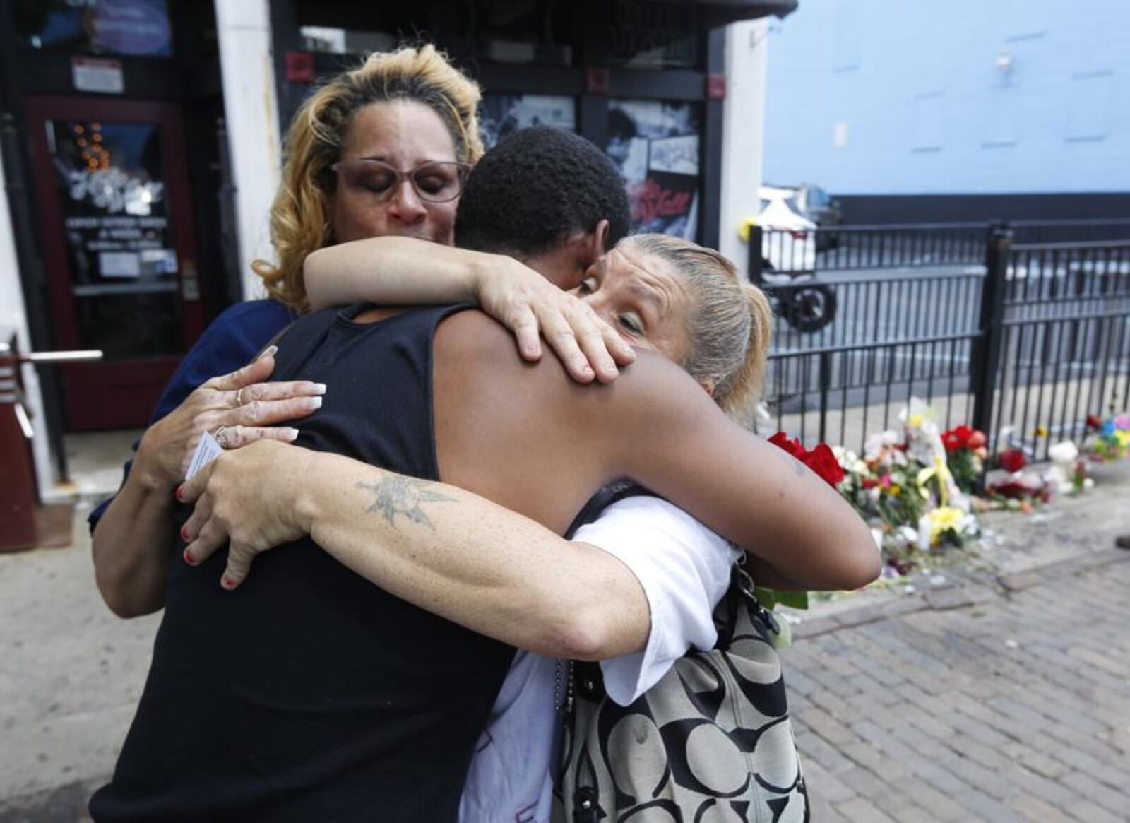 Harry Payne is hugged by Jean Davies, left, and Mary K. Curtis on East Fifth Street to leave flowers for slain friend Logan Turner who was gunned down Aug. 4 with eight other victims. TY GREENLEES / STAFF