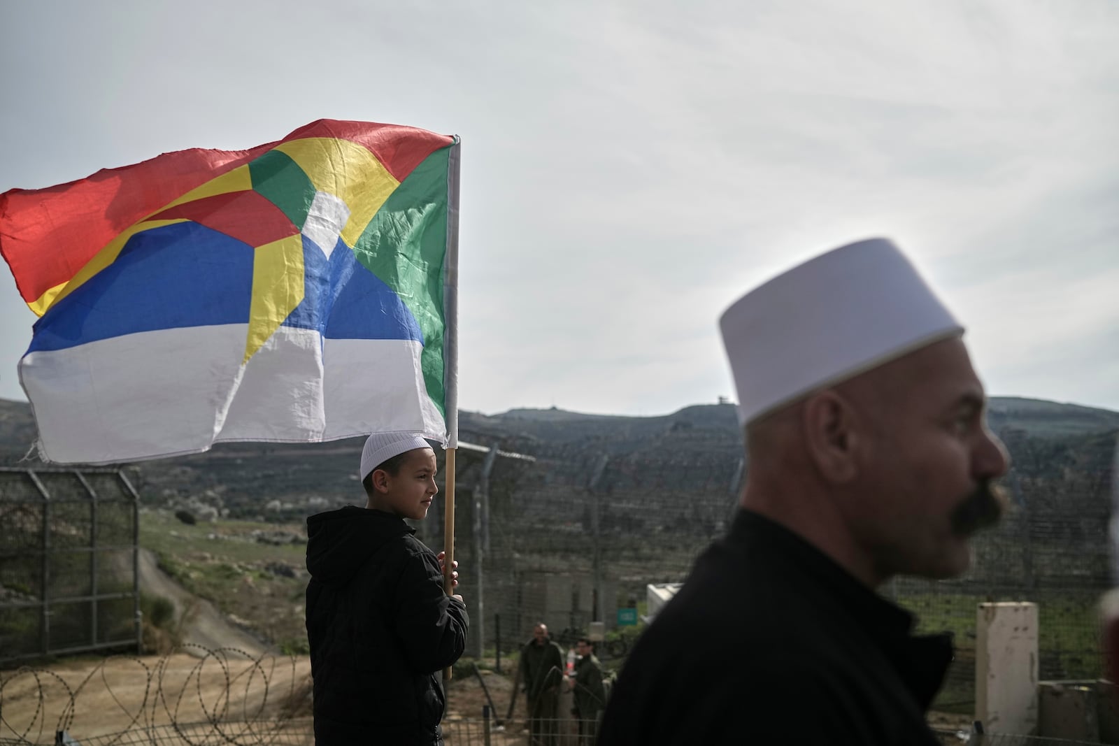 A boy holds a Druze flag as members of the Druze community and clerics wait near the border for buses carrying members of the Syrian Druze community to cross from Syria in the village of Majdal Shams, in the Israeli-controlled Golan Heights, Friday, March 14, 2025. (AP Photo/Leo Correa)