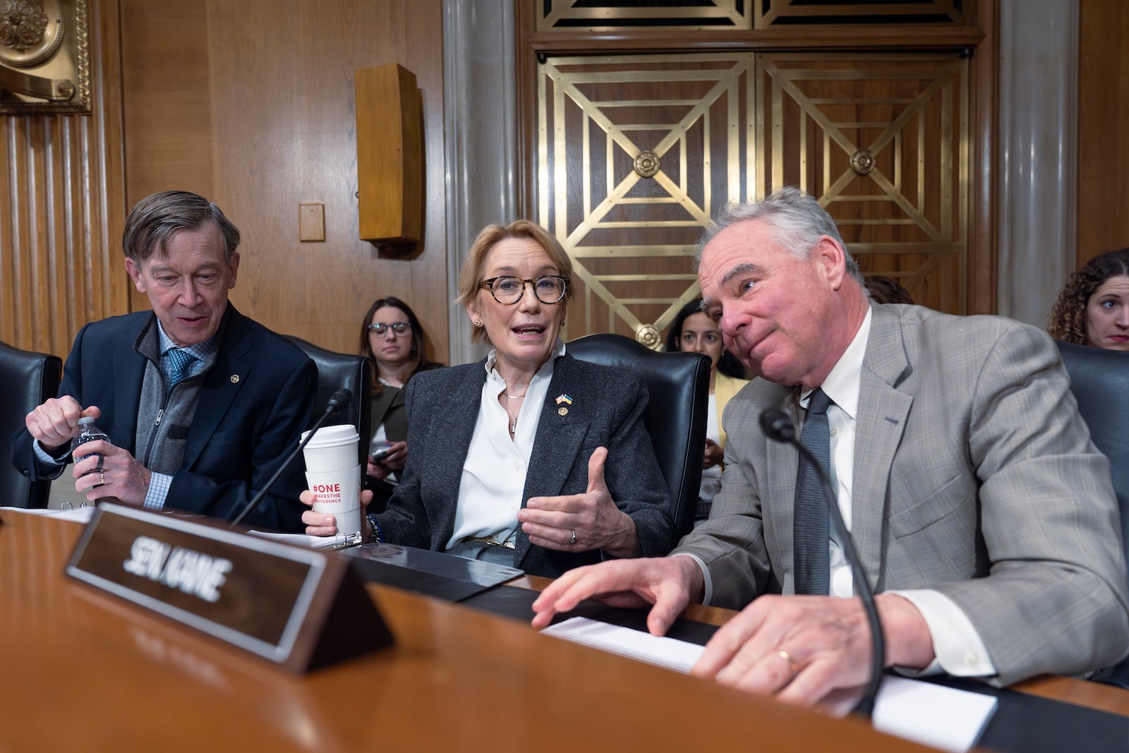 Sen. John Hickenlooper, D-Colo., from left, Sen. Maggie Hassan, D-N.H., and Sen. Tim Kaine, D-Va., talk as the Health, Education, Labor and Pensions (HELP) Committee meets to consider President Donald Trump's nominations for the director of the National Institutes of Health, and the commissioner of the Food and Drug Administration, on Capitol Hill in Washington, Thursday, March 13, 2025. (AP Photo/J. Scott Applewhite)