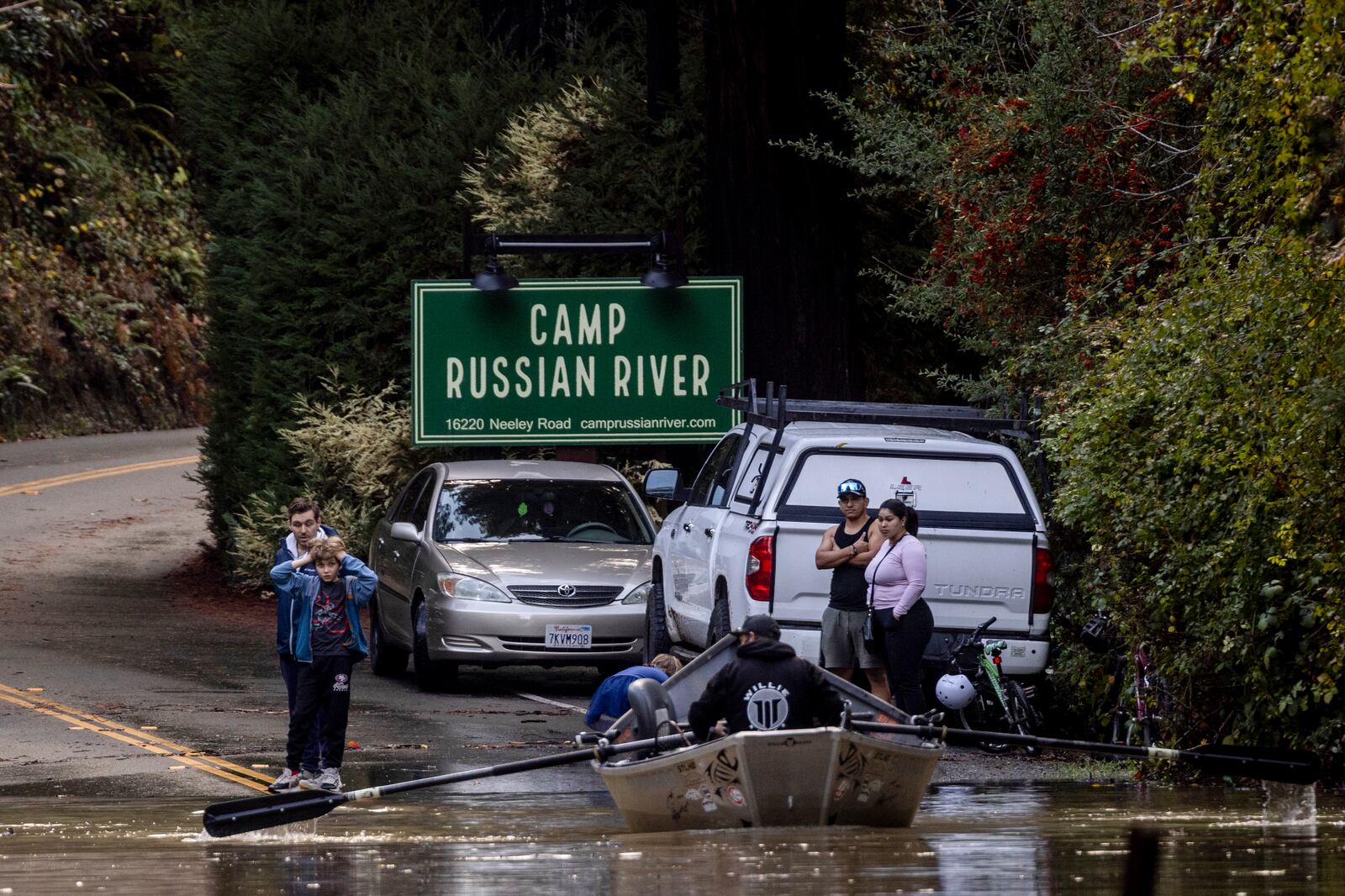 Residents watch as Ben Cote rows a boat across a flooded Neely road after a major storm in Guerneville, Calif., Saturday, Nov. 23, 2024. (Stephen Lam/San Francisco Chronicle via AP)