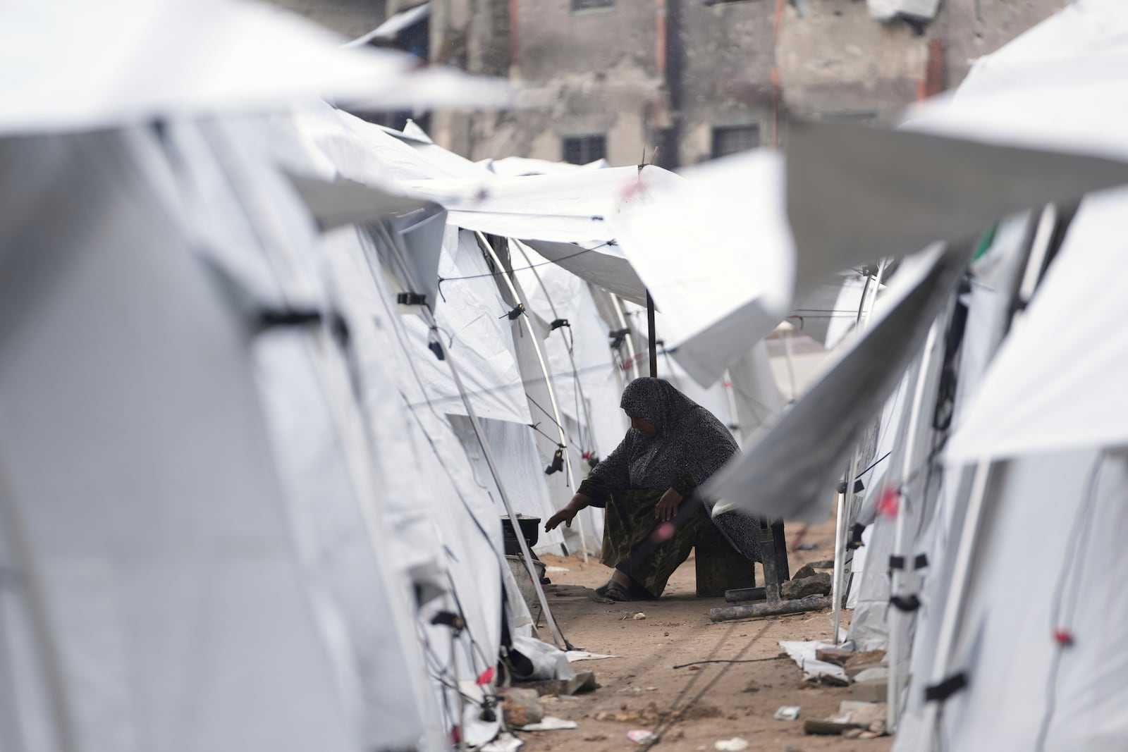 A displaced Palestinian woman cooks in a sprawling tent camp adjacent to destroyed homes and buildings in Gaza City, Gaza Strip, Saturday, March 1, 2025 during the Muslim holy month of Ramadan. (AP Photo/Abdel Kareem Hana)