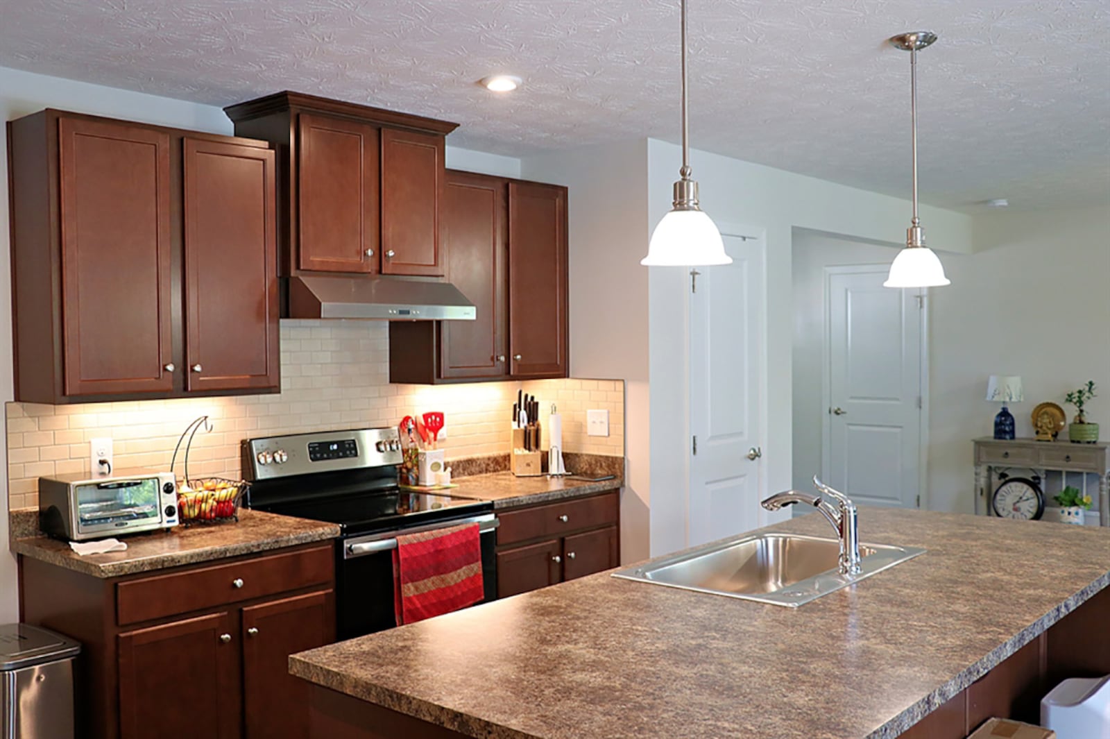 1021 Colonial WaAn island provides additional work space within the kitchen plus allows for breakfast bar seating. The island has a sink and storage and is within steps of the wall cabinetry that surrounds the range. Walnut cabinets compliment the lighter countertops. CONTRIBUTED PHOTO BY KATHY TYLER