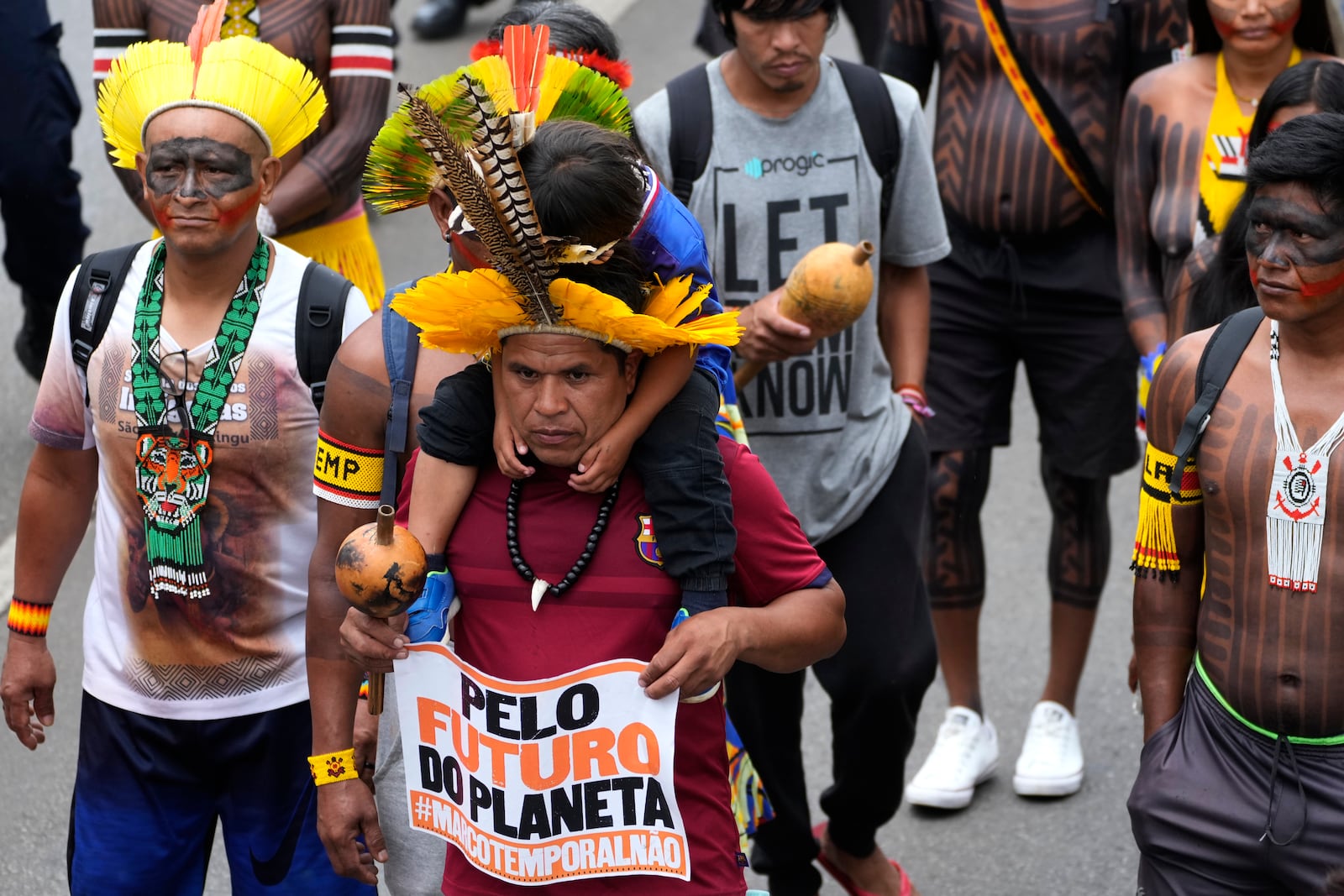 An Indigenous father carries his son on his shoulder, holding a sign with a message that reads in Portuguese: "For the Planet's Future", during a protest against the prospective creation of a benchmark time limit that threatens to strip some of Indigenous lands, in Brasilia, Brazil, Wednesday, Oct. 30, 2024. (AP Photo/Eraldo Peres)