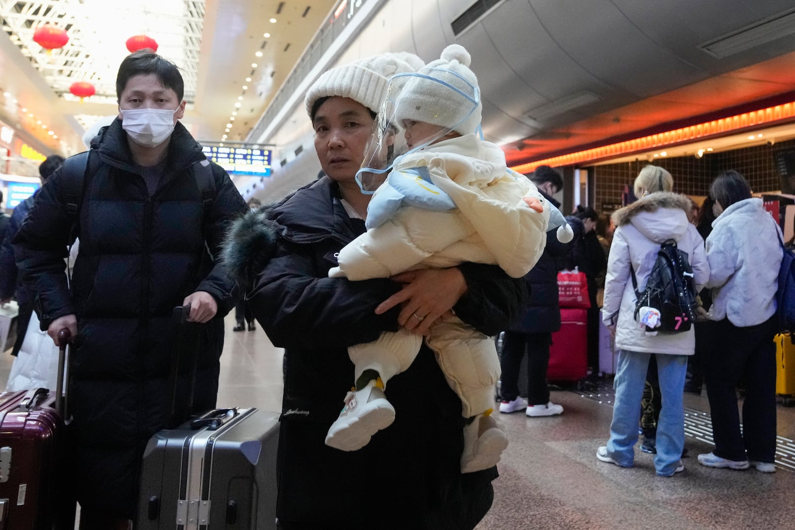 A traveler carries a baby at the departure hall as they try to catch their trains at the Beijing West Railway Station ahead of the Lunar New Year in Beijing on Friday, Jan. 24, 2025. (AP Photo/Aaron Favila)