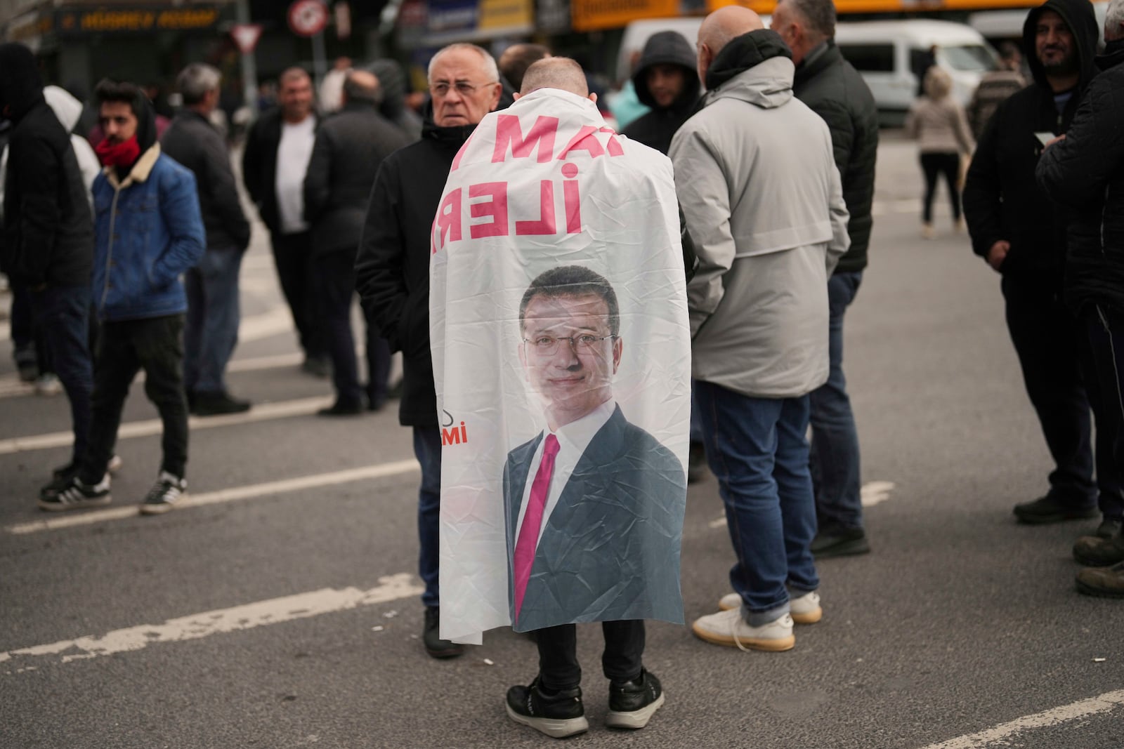 A man wears a banner featuring a photo of Istanbul Mayor Ekrem Imamoglu as he and others protest outside the Vatan Security Department, where Imamoglu is expected to be taken following his arrest in Istanbul, Turkey, on Wednesday, March 19, 2025. (AP Photo/Francisco Seco)