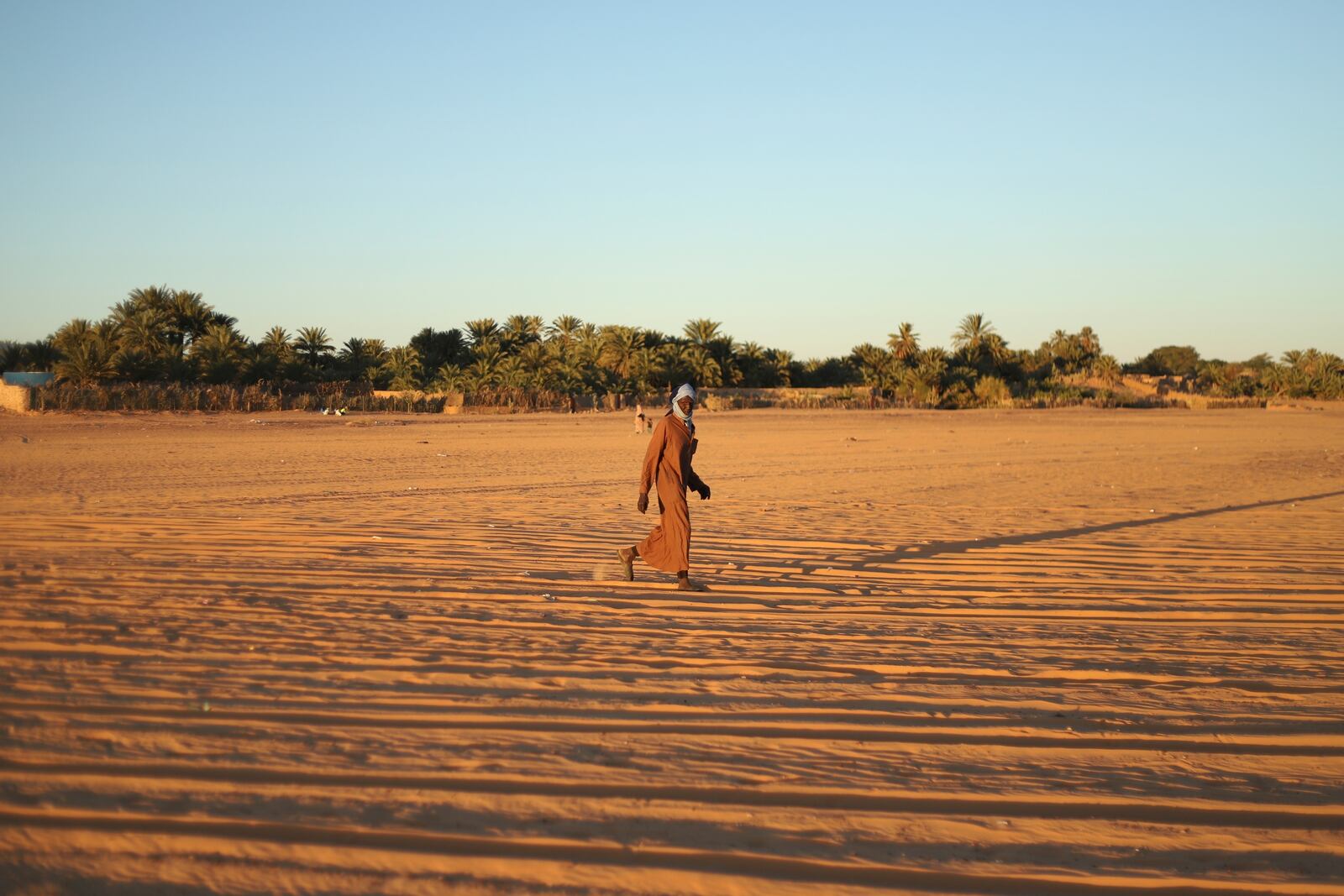 A man walks through sand with palm trees in the distance in Chinguetti, Mauritania on Feb. 3, 2025. (AP Photo/Khaled Moulay)