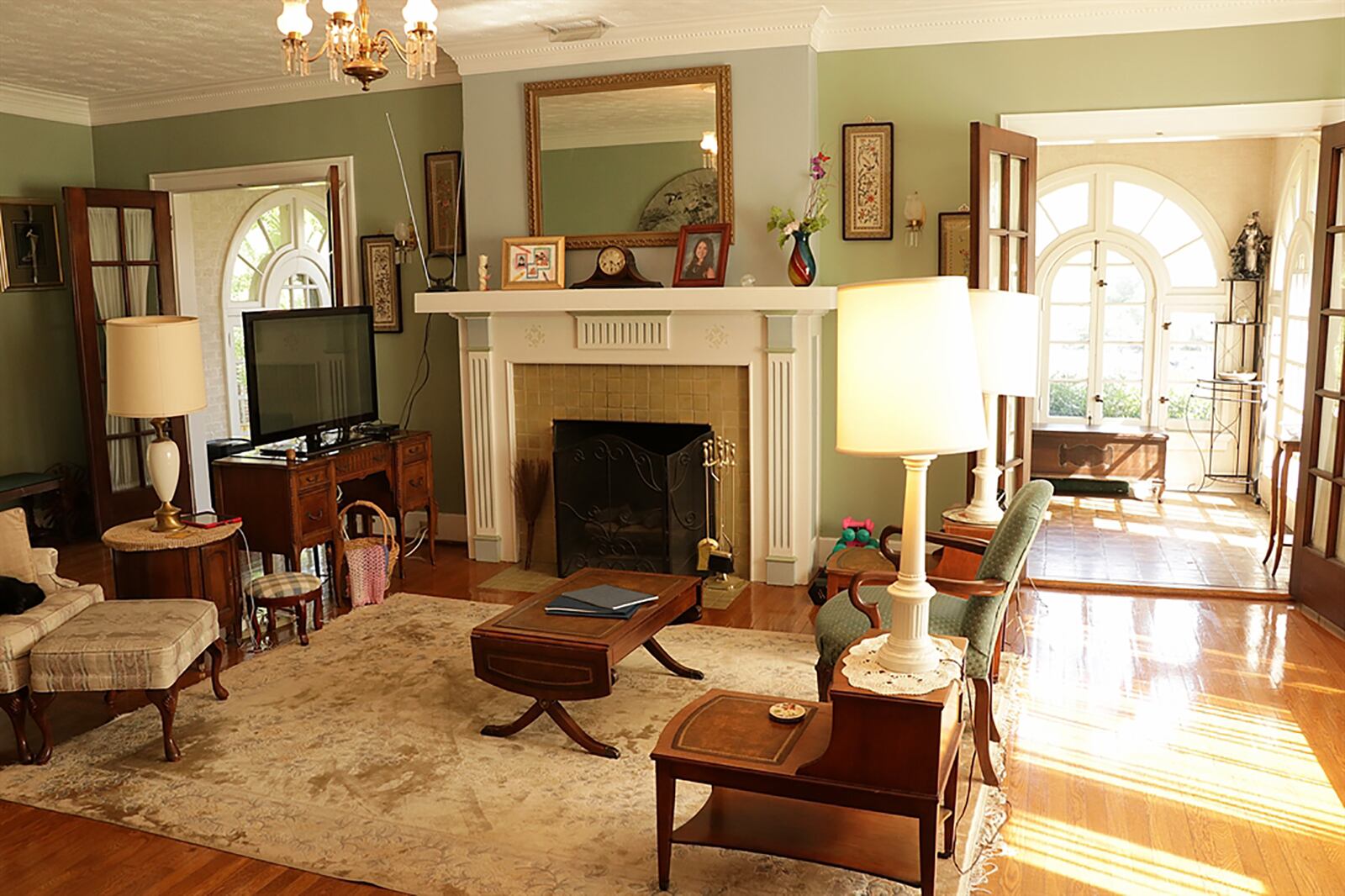 The living room has a fireplace with fluted wood mantel and stone surround and hearth. Two sets of tall French doors open to a solarium, which has tile flooring. CONTRIBUTED PHOTO BY KATHY TYLER