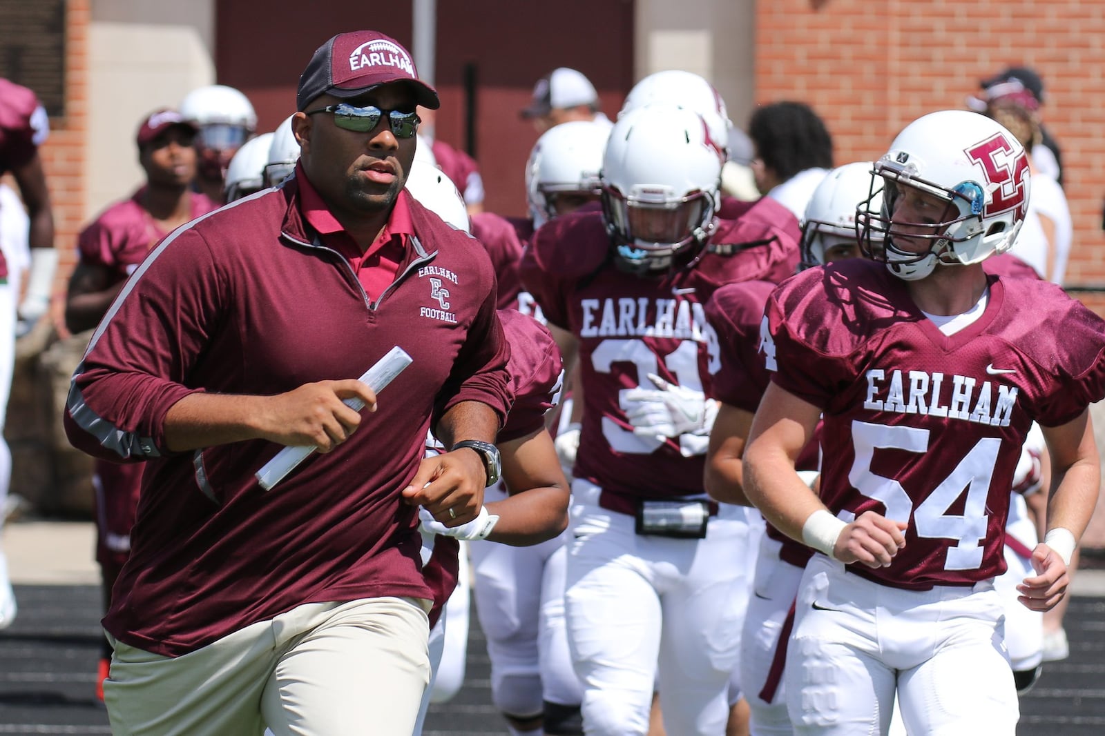 Earlham College football coach Nick Johnson runs onto the field with his team. CONTRIUBUTED PHOTO