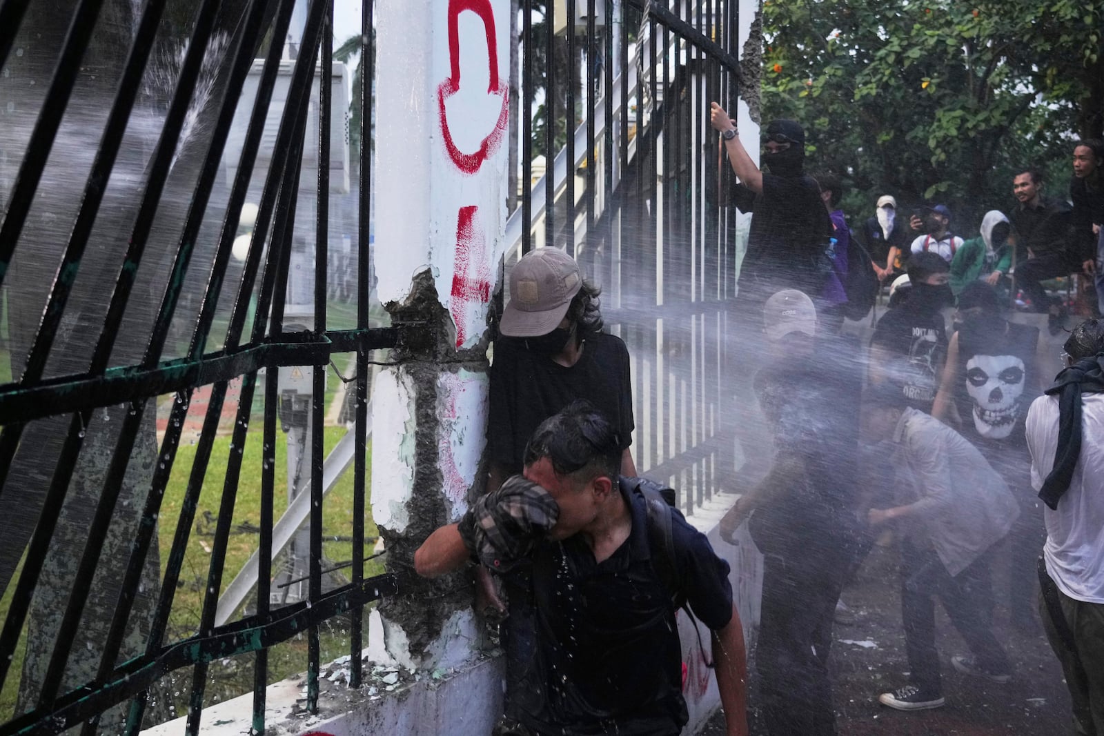 Protesters take cover as police use a water cannon during a rally in Jakarta, Indonesia, Thursday, March 20, 2025, against the passing of a controversial revision of a military law that will allow military officers to serve in more government posts without resigning from the armed forces. (AP Photo/Tatan Syuflana)